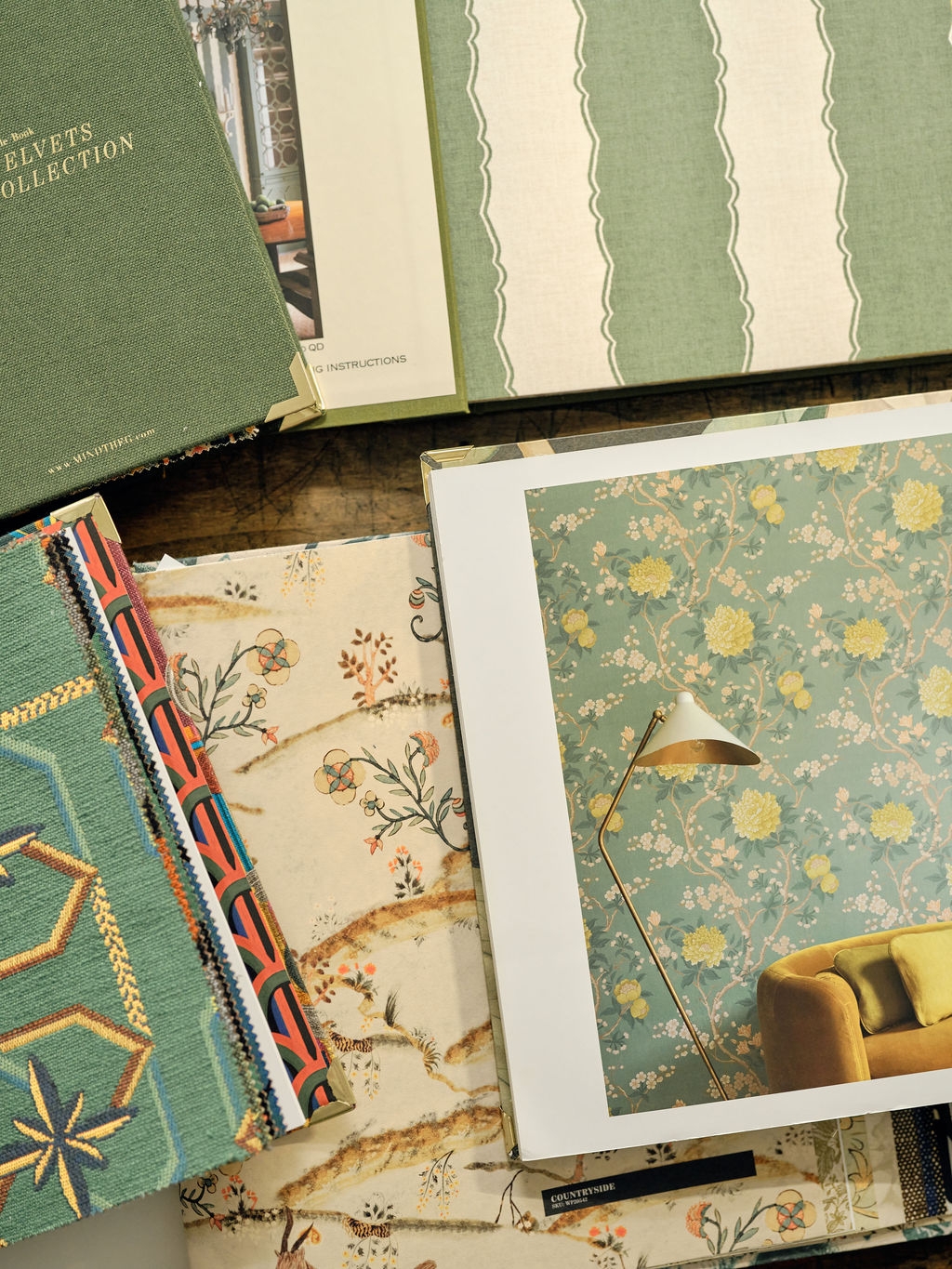 Stack of open sample books with green velvet, striped and floral wallpaper swatches