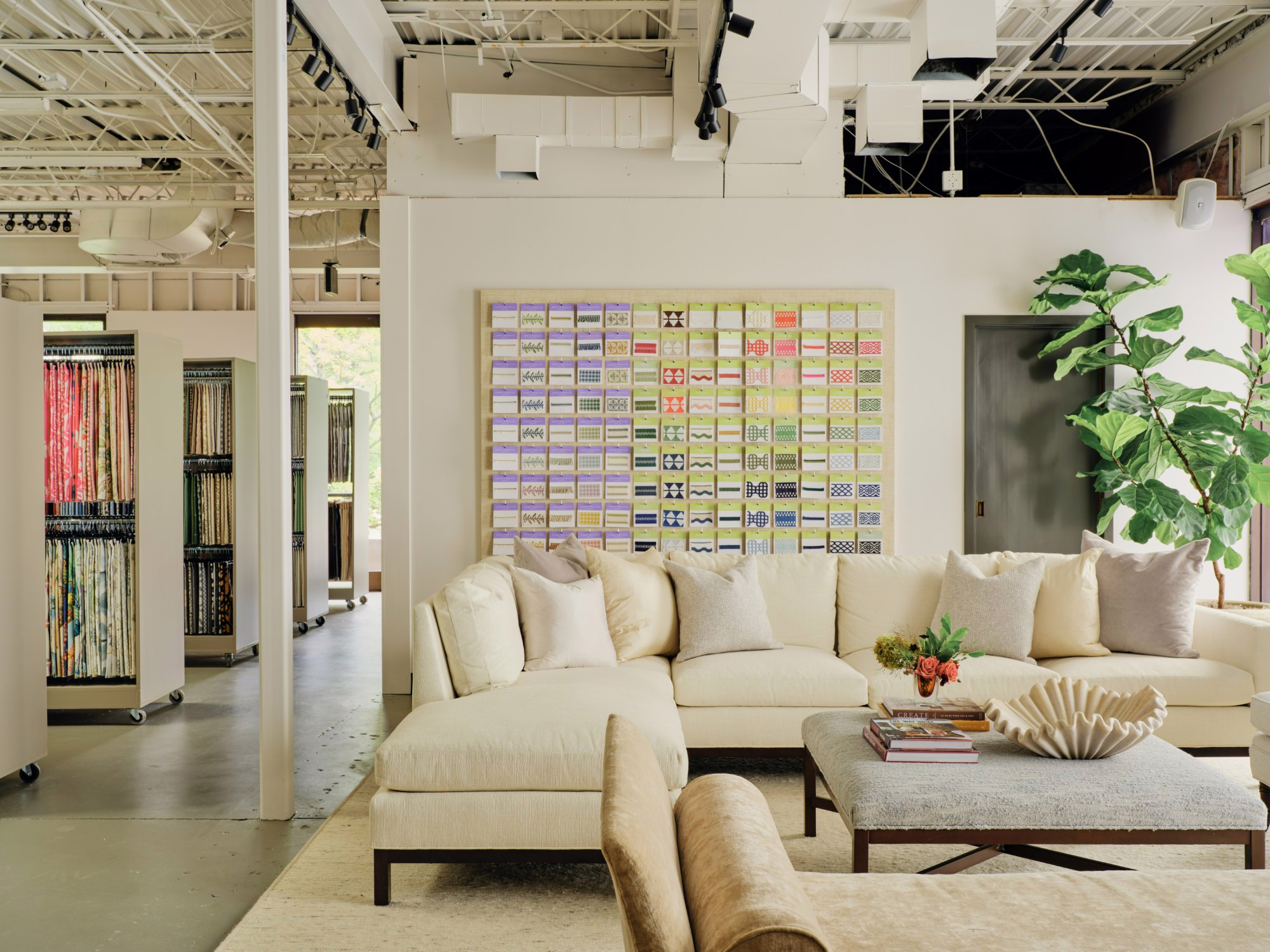 Showroom seating area with a cream sectional, plants and a wall of fabric samples