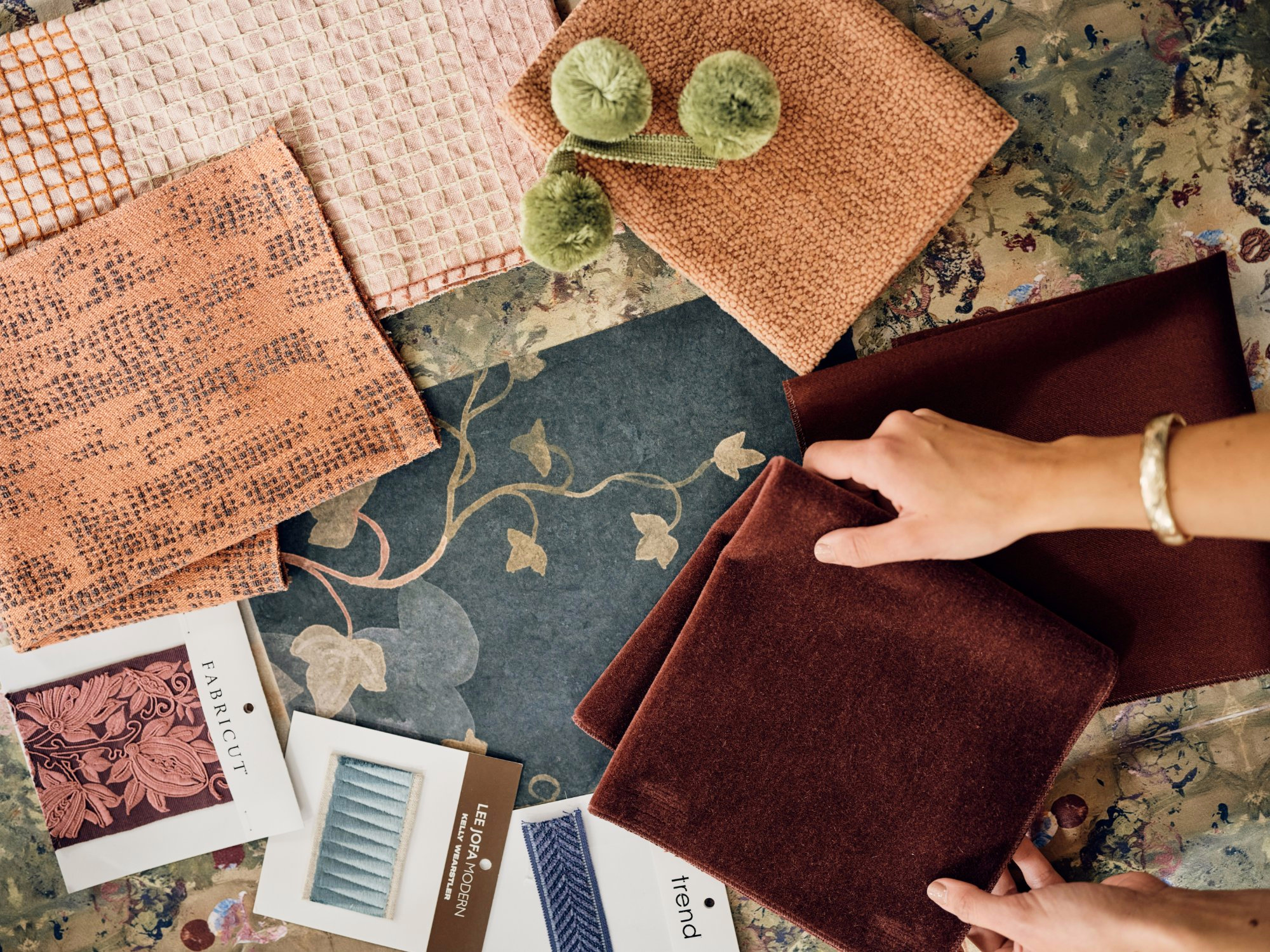 Hand holding a burgundy velvet swatch over a spread of textile and rug samples
