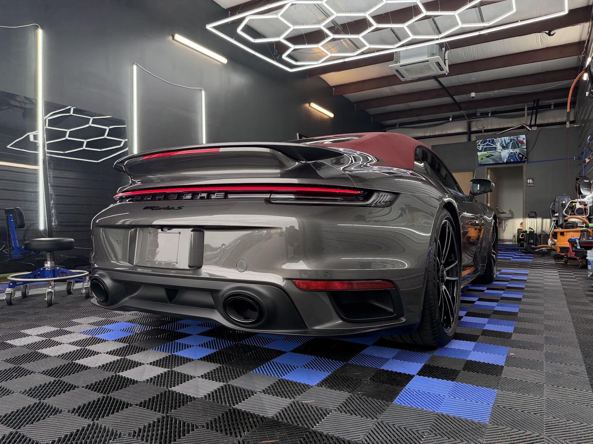 Rear of a gray Porsche 911 Turbo S with a ceramic coating and window tint under hexagon garage lights