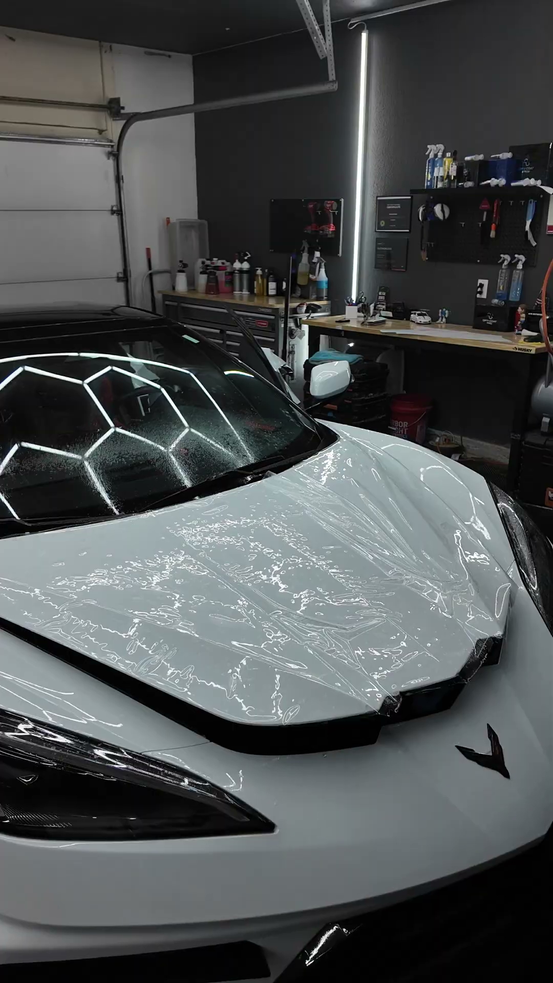 Full body paint protection film being installed on a white C8 Corvette hood under hexagon lights