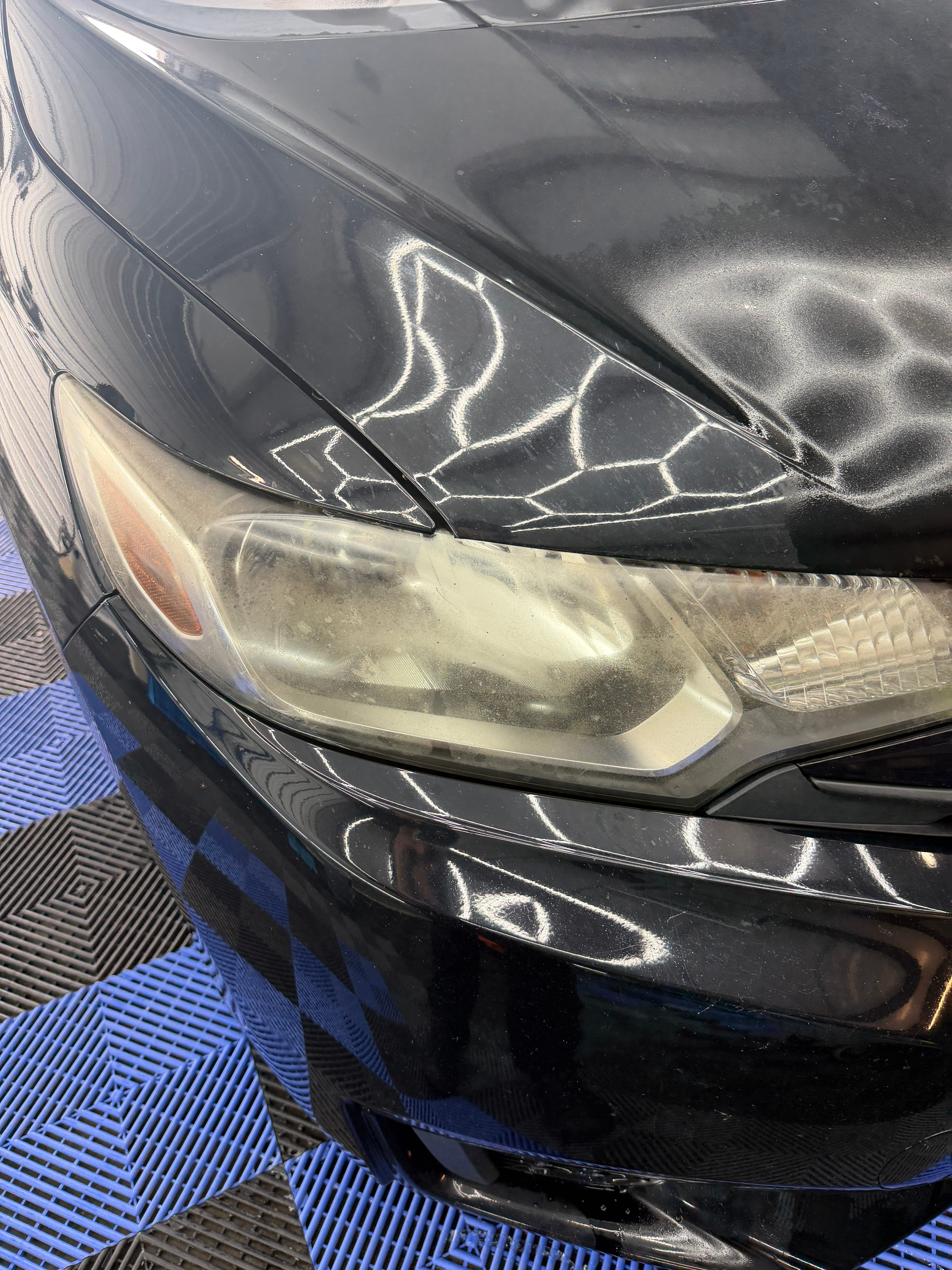 Yellowed, hazy headlight on a black car before headlight restoration at Detail Armor