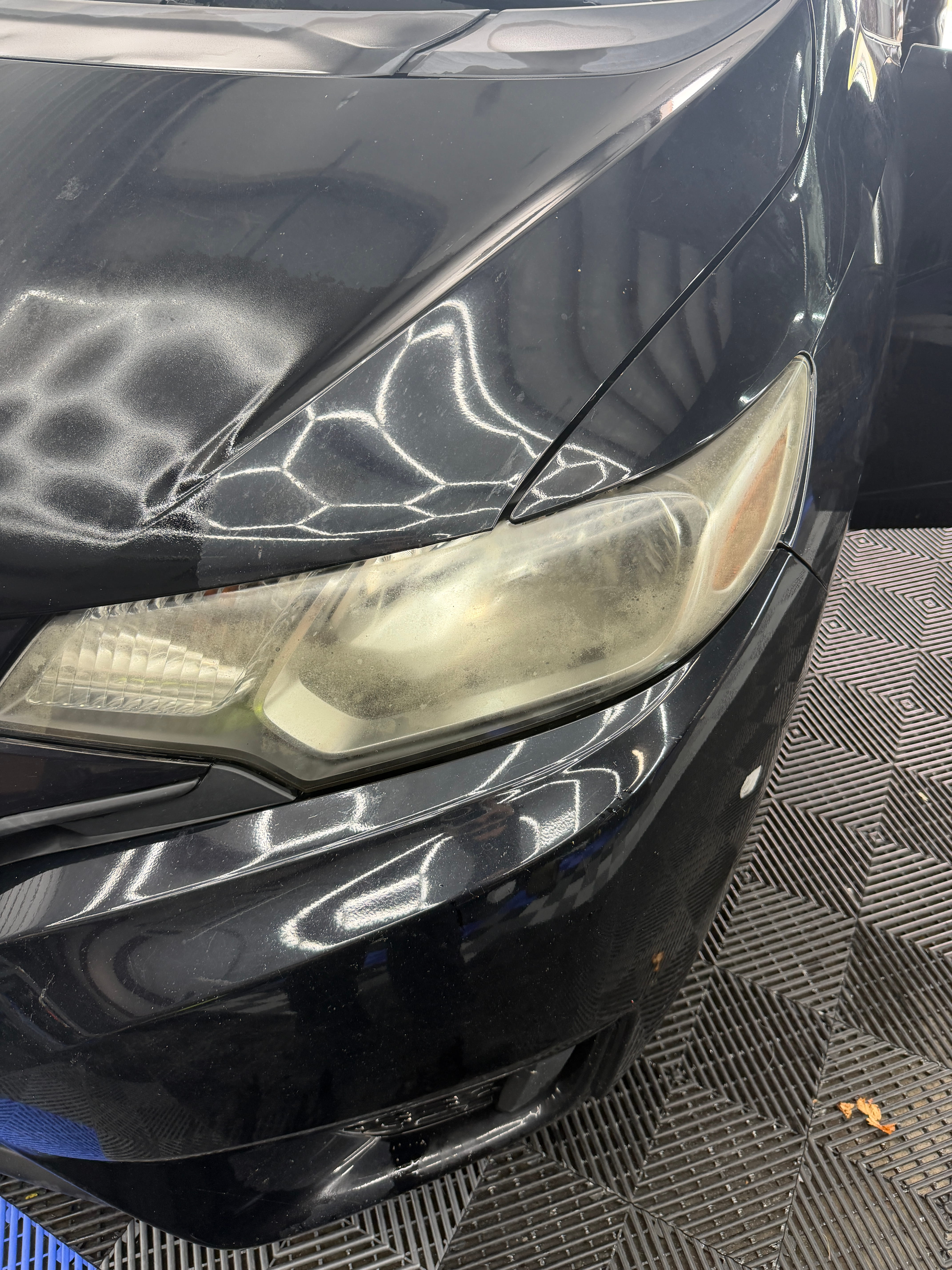 Faded, oxidized headlight on a black car before headlight restoration at Detail Armor