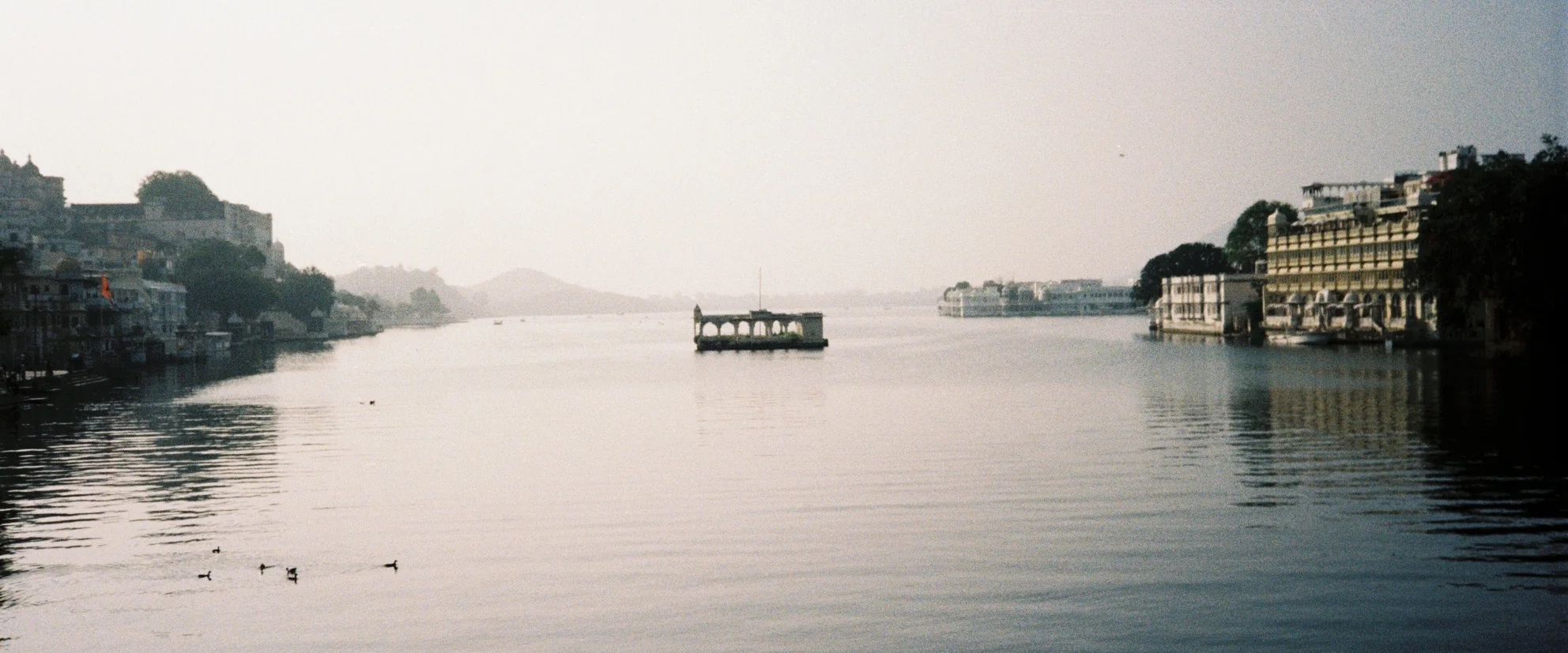 A wide, hazy stretch of still water with buildings along both shores and a small boat near the centre.