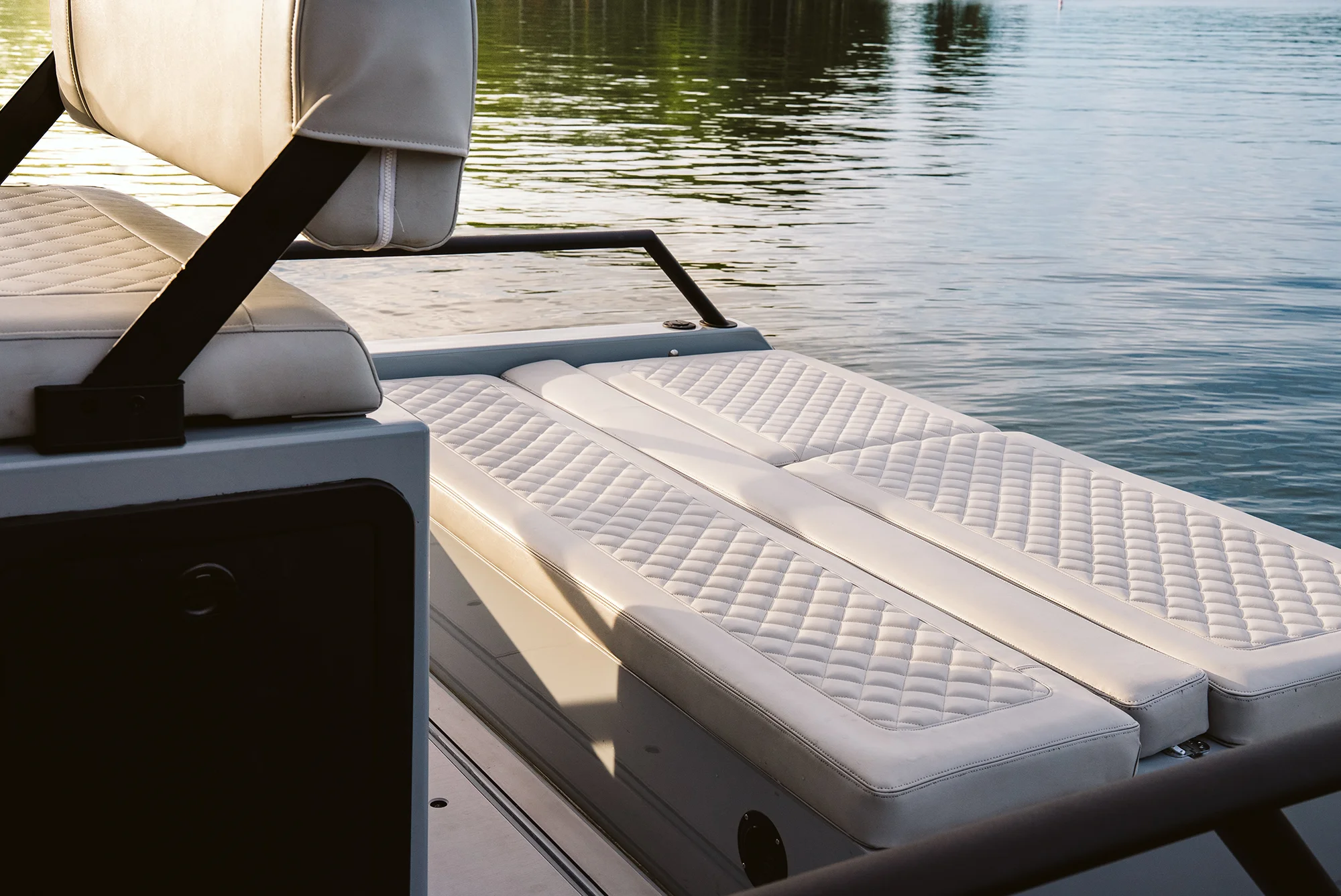 Close-up of white cushioned seating area on a boat with calm water in the background.