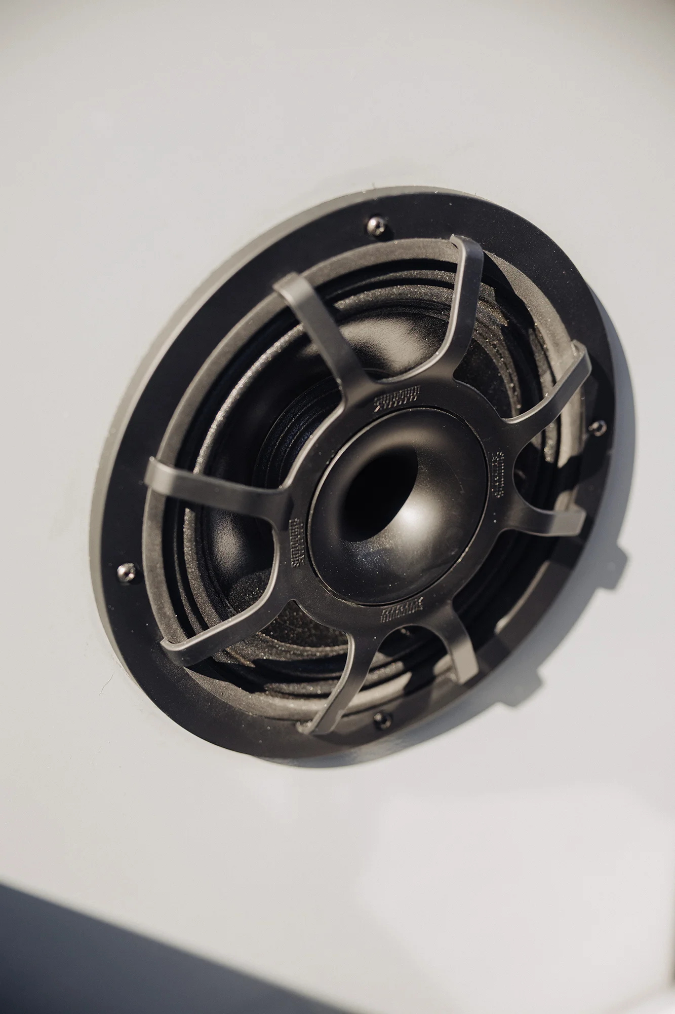 Close-up of a black speaker mounted on a white surface with a protective grille featuring six spokes.