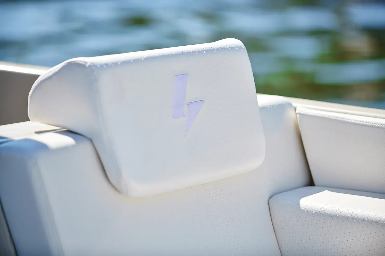 White cushioned boat seat with a headrest featuring a subtle lightning bolt logo, water blurred in the background.