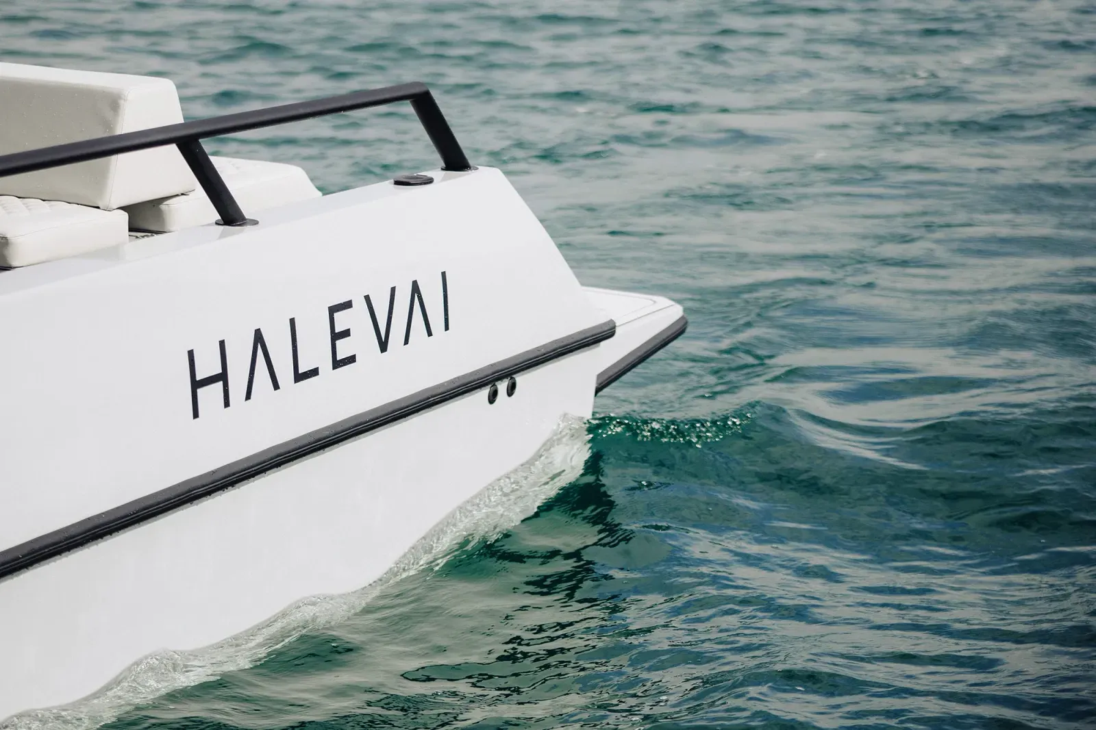 Close-up of the rear side of a white boat on green-blue water with the word 'HALEVAI' in black letters on the boat's hull.
