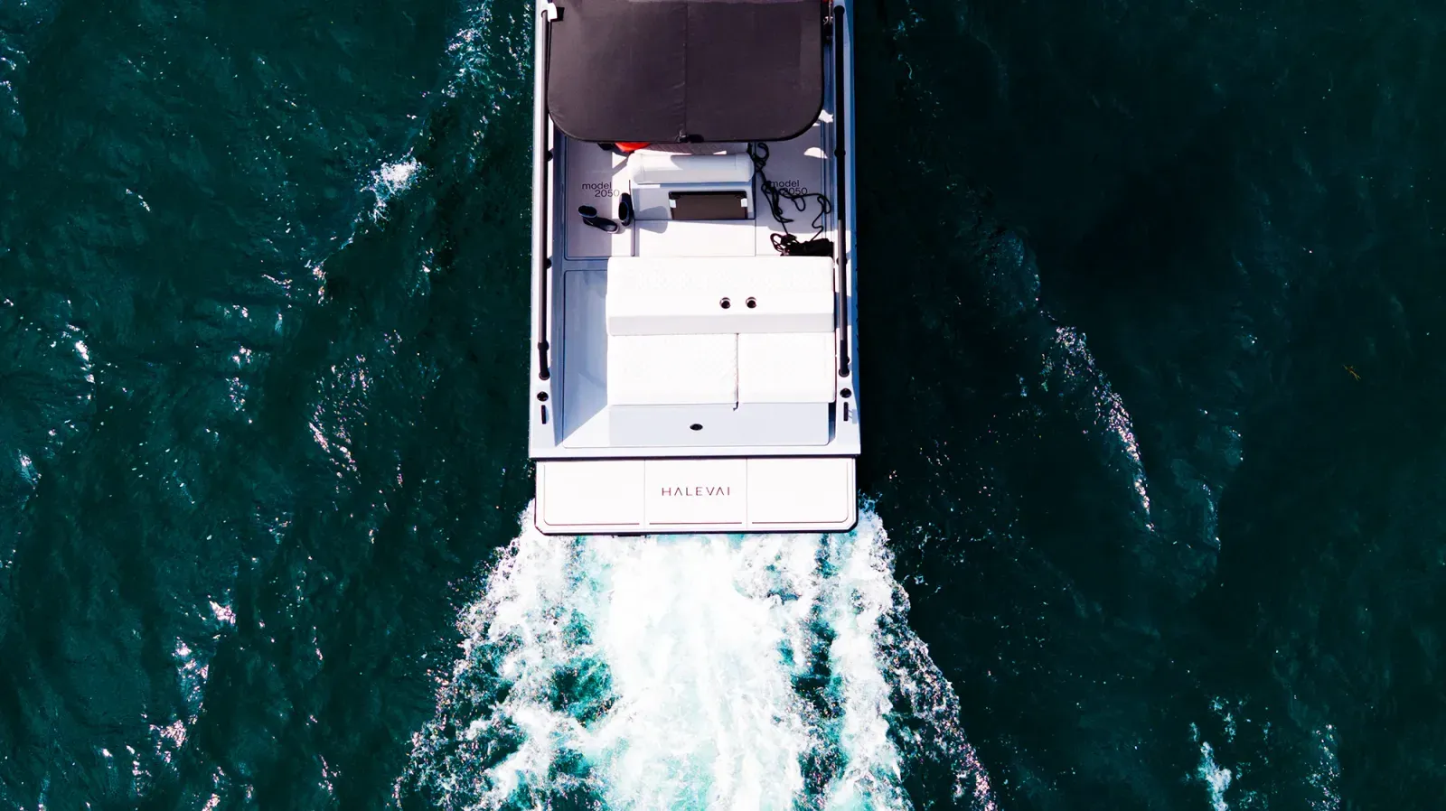 Overhead view of a white boat named HALEVAI moving through dark blue water with white waves trailing behind.