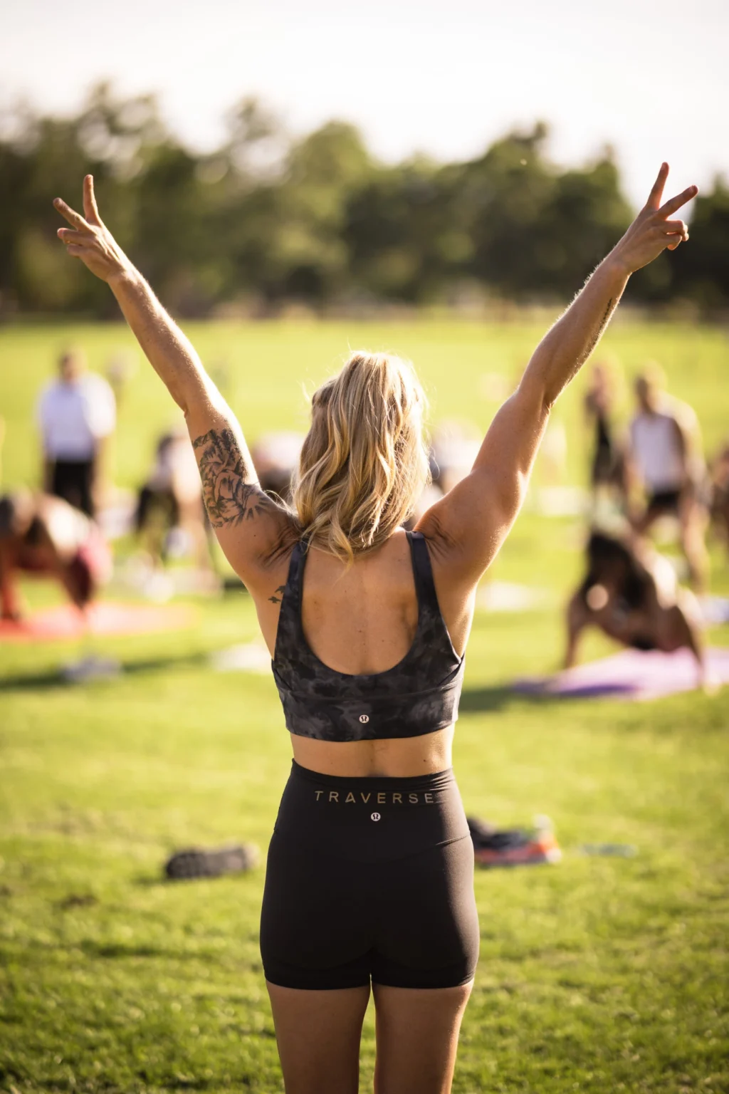 An instructor leading an outdoor group with both arms raised.
