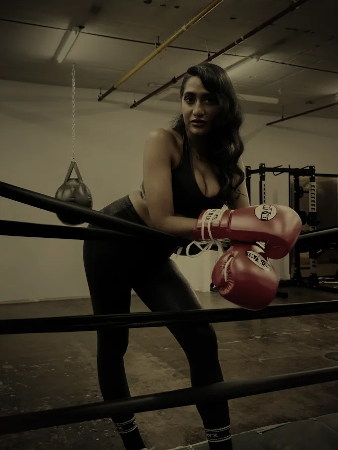 A boxer in red gloves leans on the ring ropes