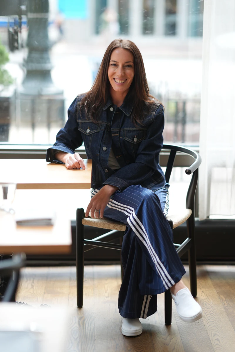 Erin Schirack smiling, seated in a chair by a bright window.