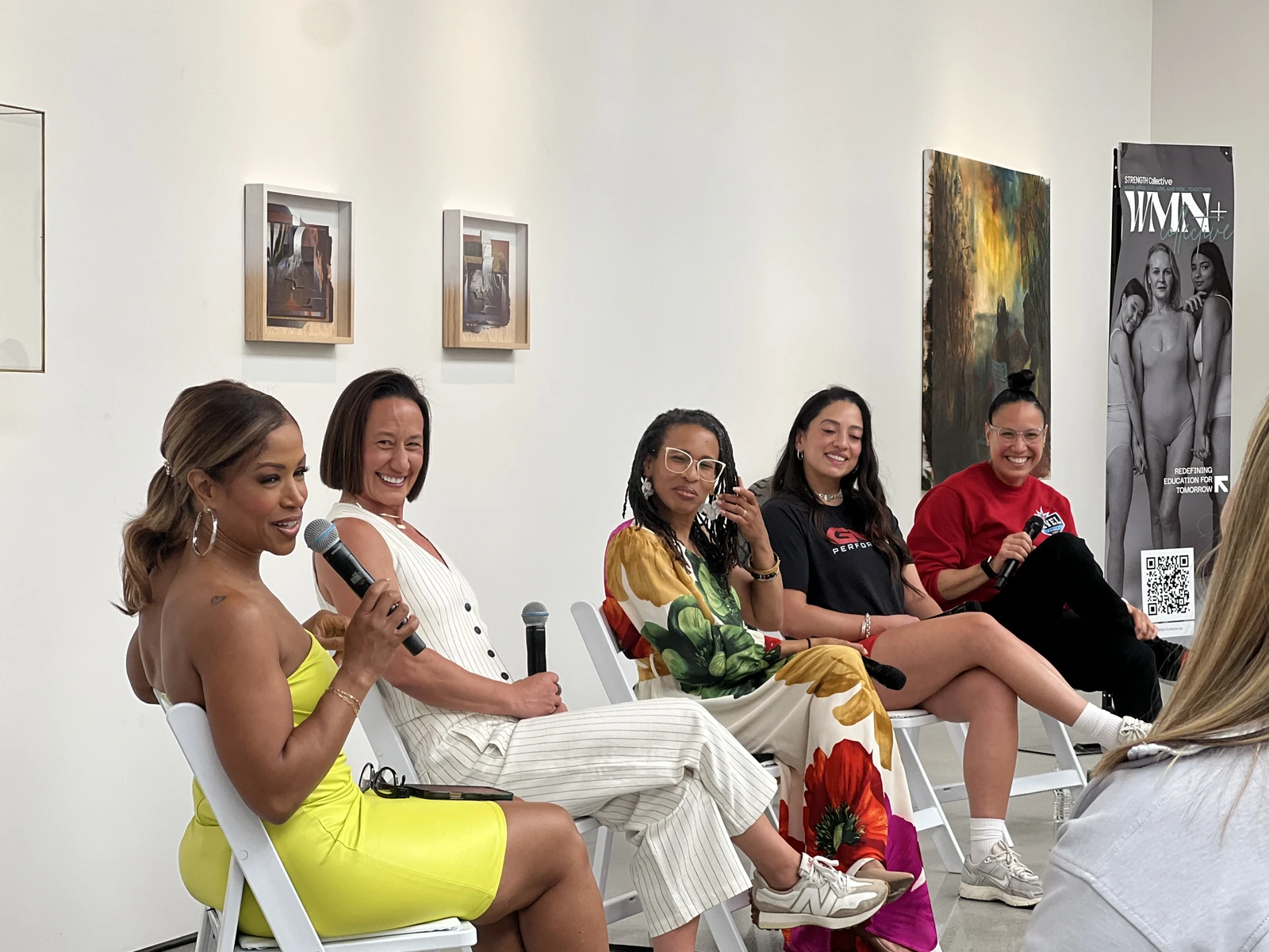 Five women seated on a panel, with a speaker holding a microphone.
