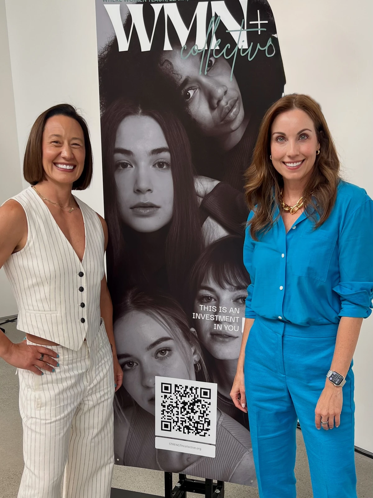 Two women in light and blue outfits standing beside a WMN+ Collective banner.