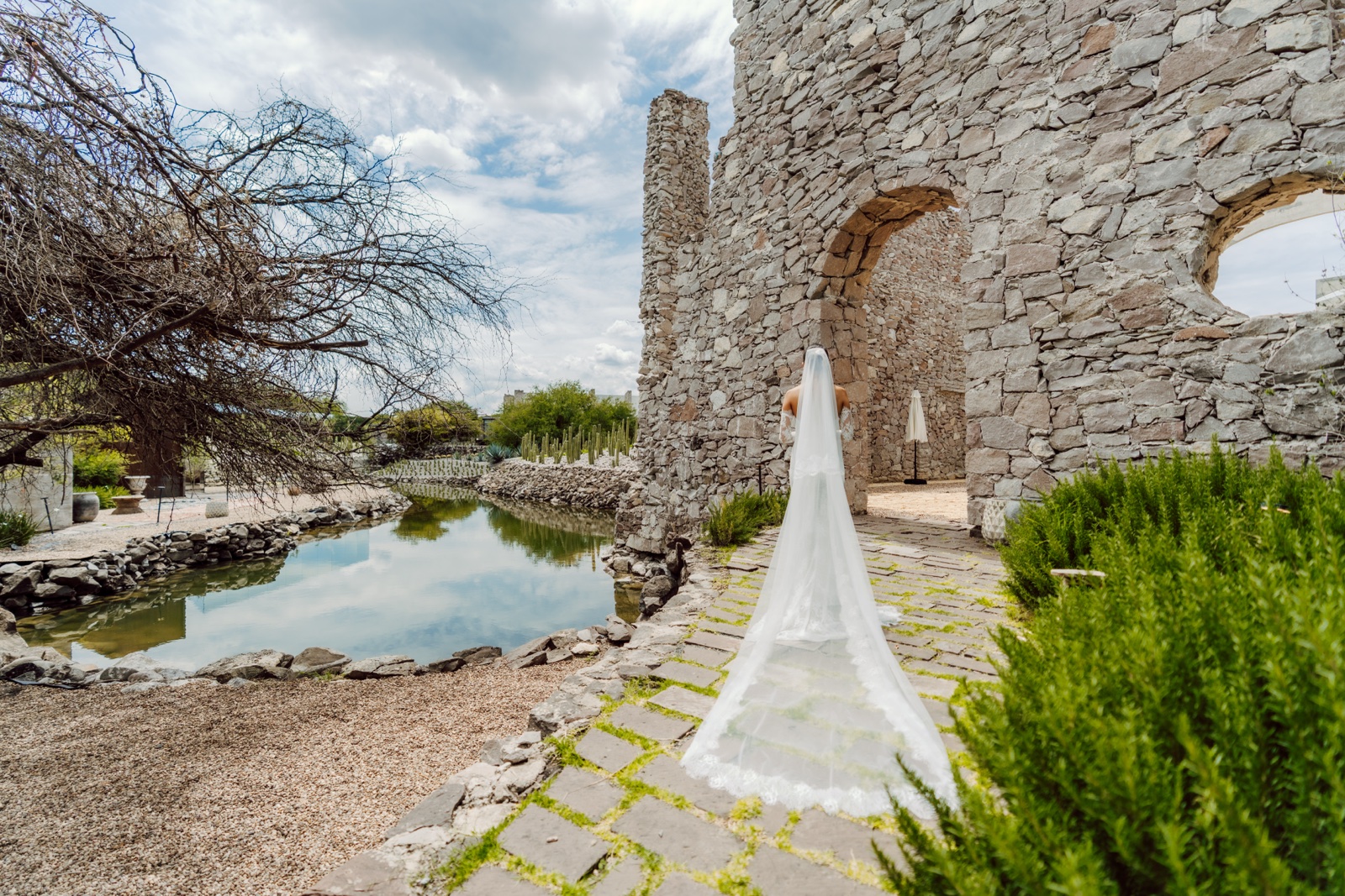 novia de pie junto a un arco de piedra en el jardín