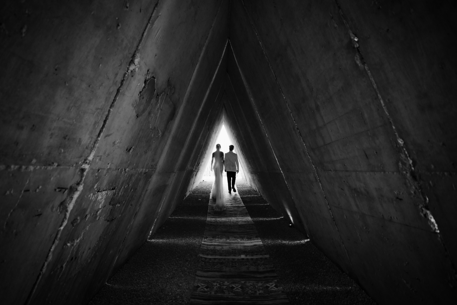 novios bajo una estructura triangular entre cactus, en blanco y negro