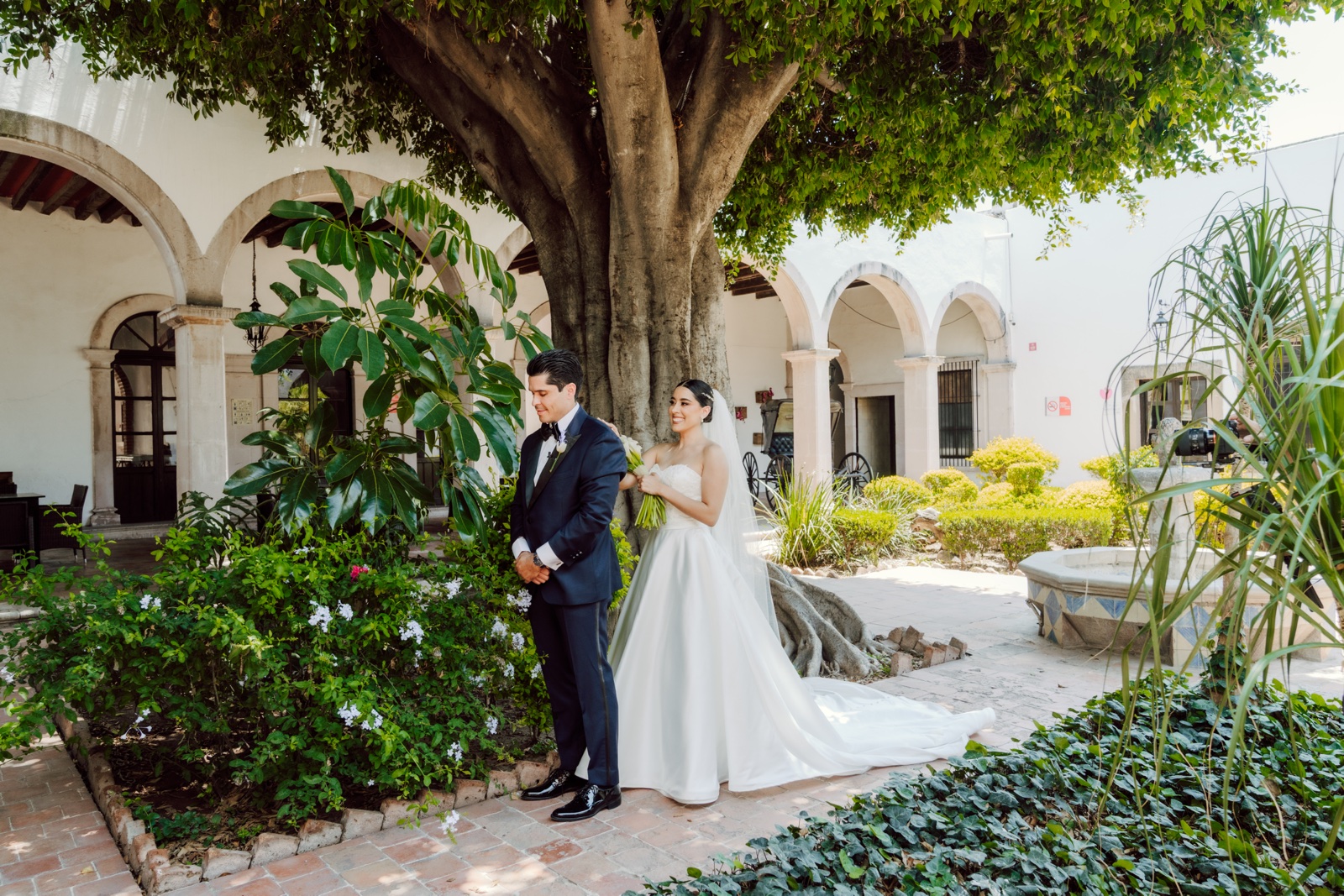 novios posando junto a un árbol en el patio