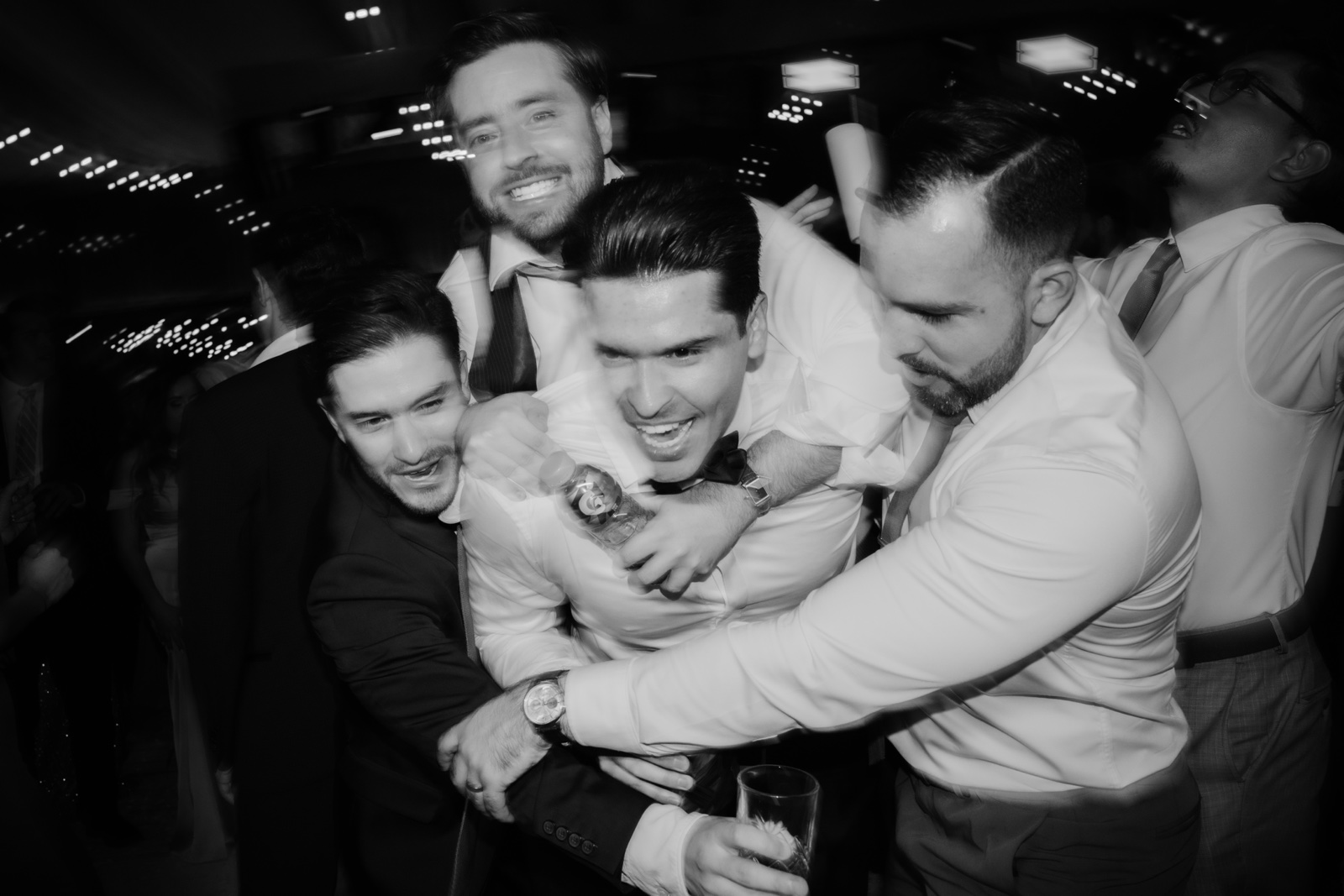 novio abrazado por invitados en la fiesta, en blanco y negro
