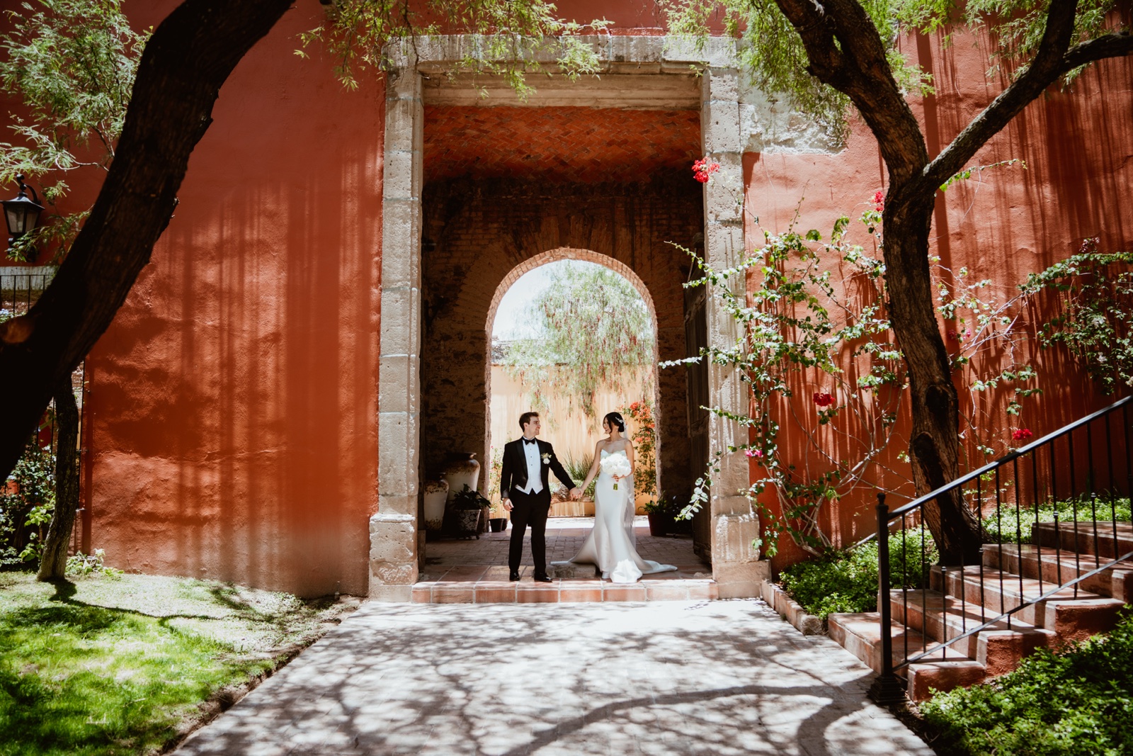 novios bajo un arco de piedra en un patio de muros rojizos