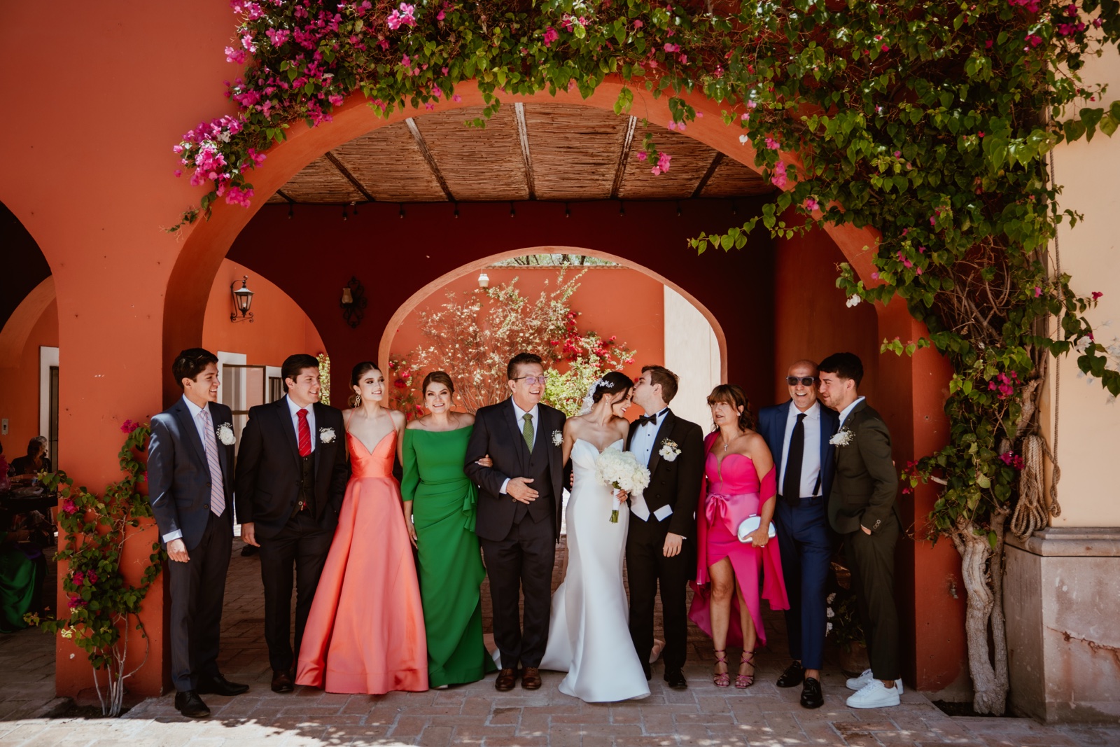 grupo de invitados posando bajo un arco de muros rojizos