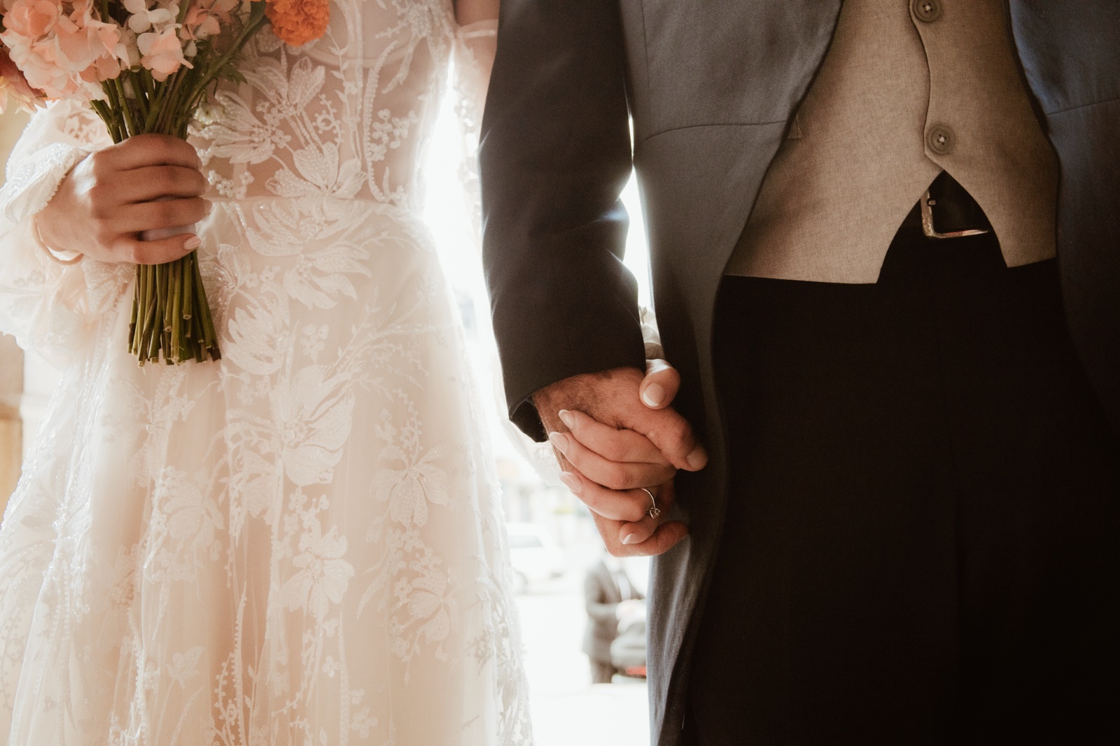 detalle del vestido y traje de los novios tomados del brazo
