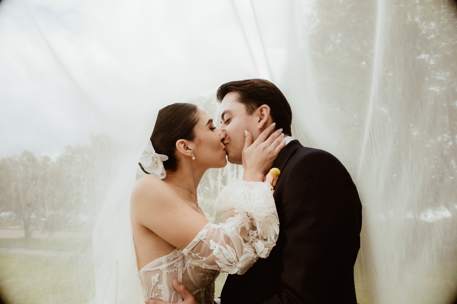 novios besándose frente a una cortina blanca
