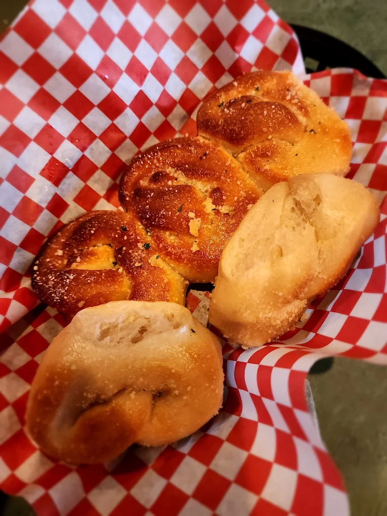 Basket lined with red and white checkered paper holding four golden brown soft pretzels with coarse salt and seasoning sprinkled on top.