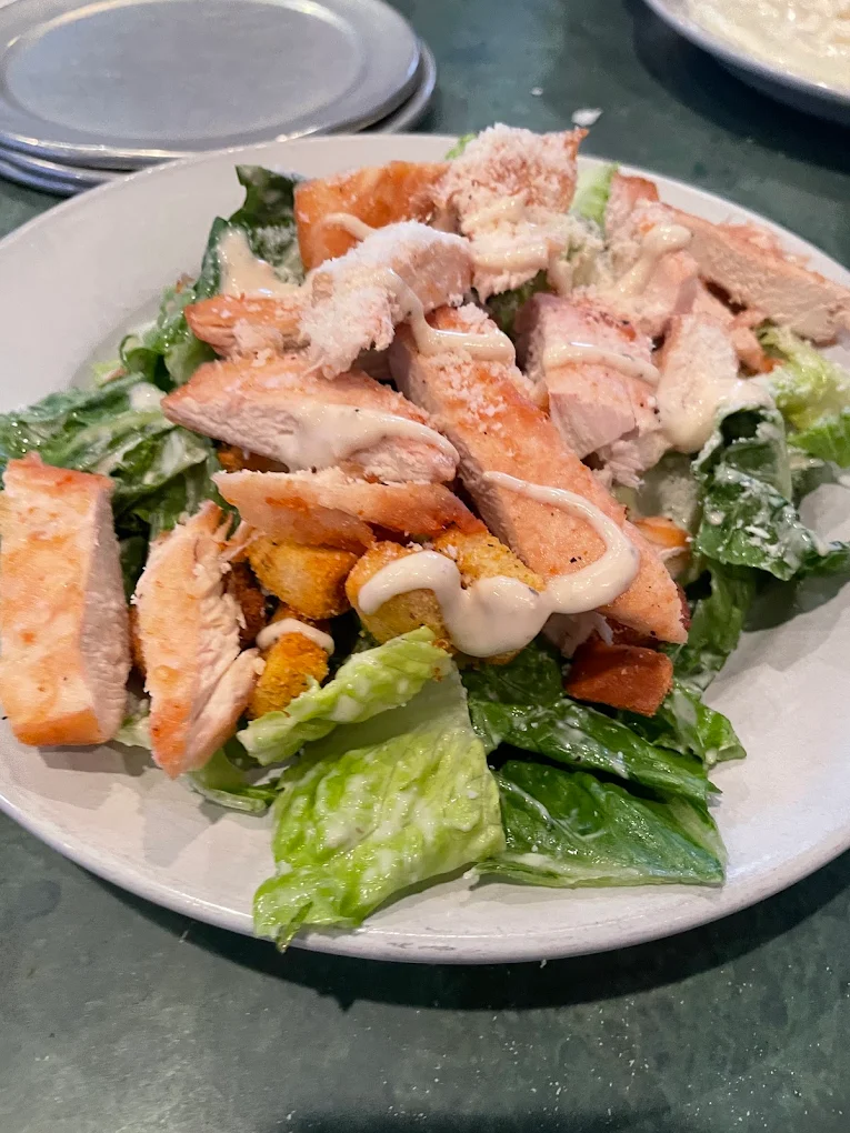 Plate of Caesar salad topped with grilled chicken strips, crispy croutons, romaine lettuce, grated cheese, and drizzled with creamy dressing.
