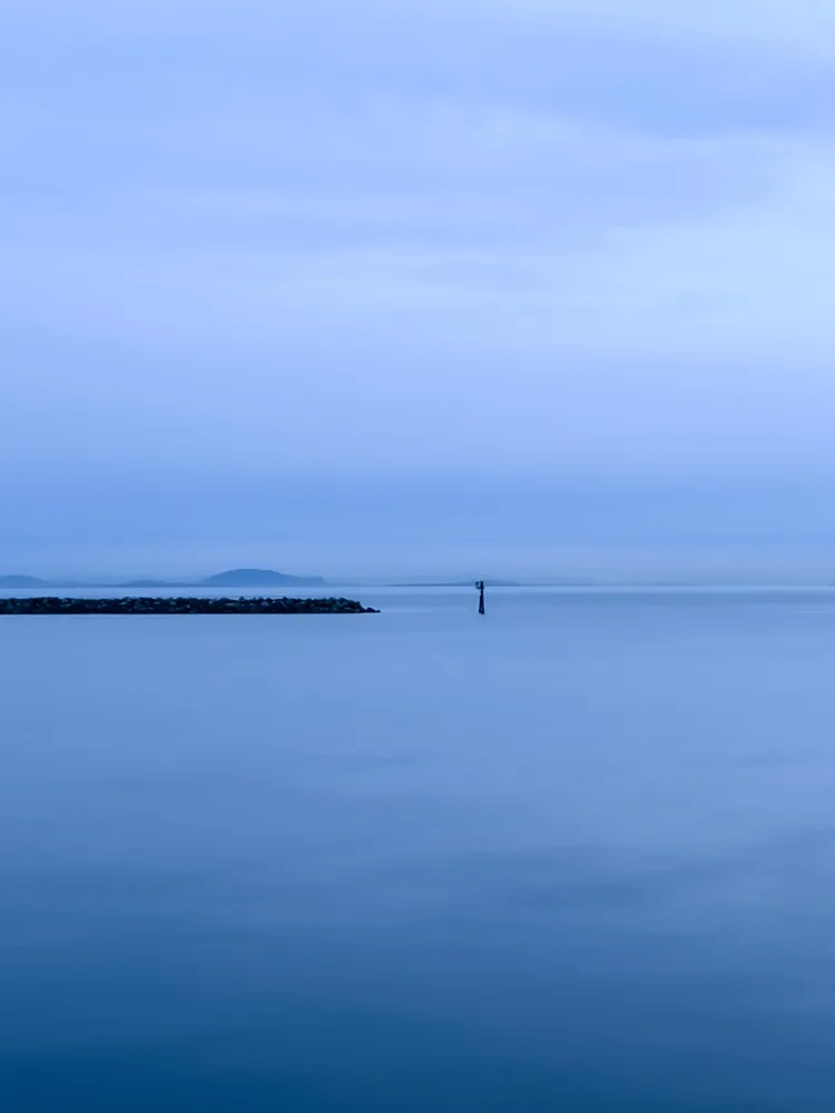 Calm blue ocean meeting a pale blue sky with a faint distant island on the horizon
