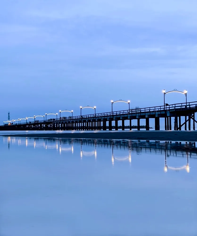 Pier lit with lamps stretching over calm blue water at dusk with soft reflections