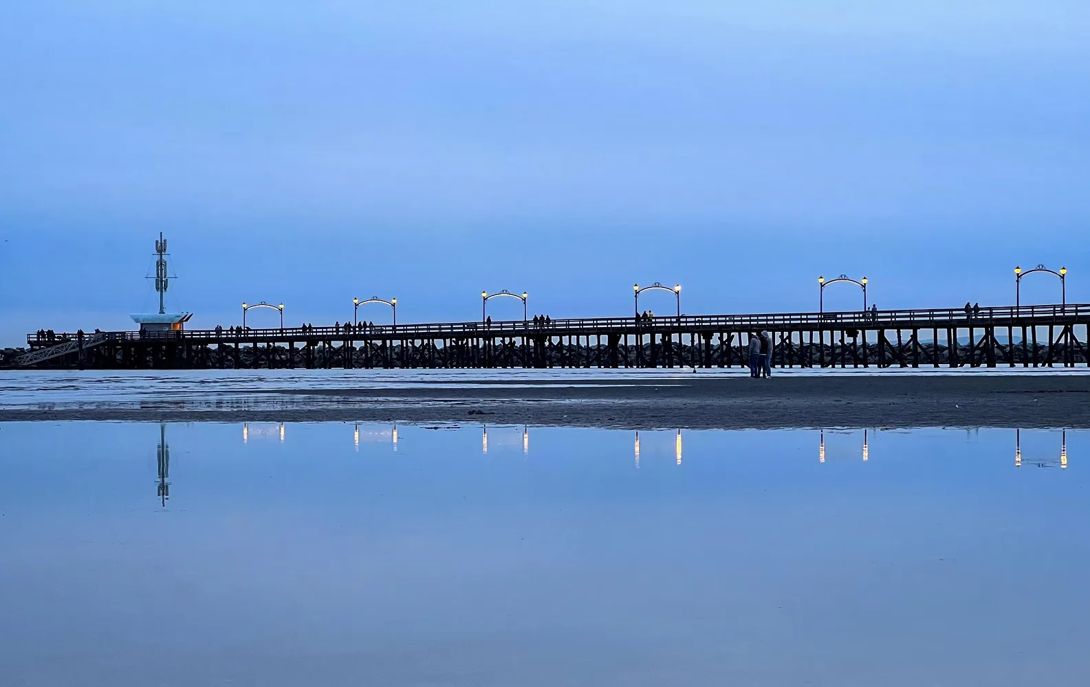 Long wooden pier silhouetted over calm reflective water during the blue hour