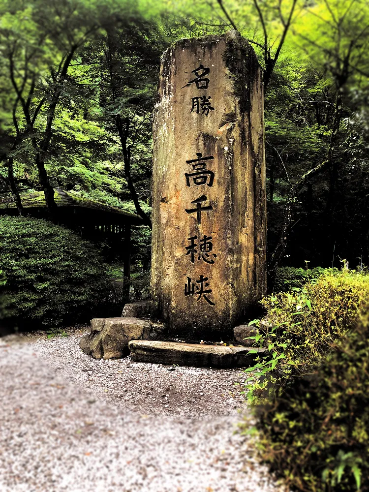 Carved wooden marker at the entrance to Takachiho Gorge surrounded by lush green forest