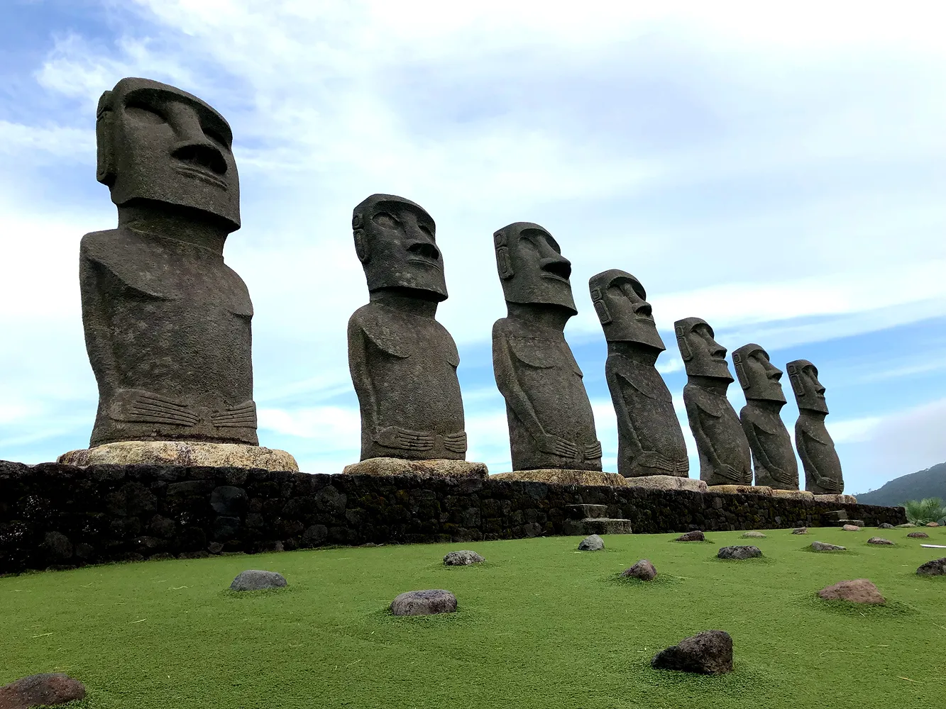 Row of seven moai statues standing on a green lawn under a blue sky in Japan