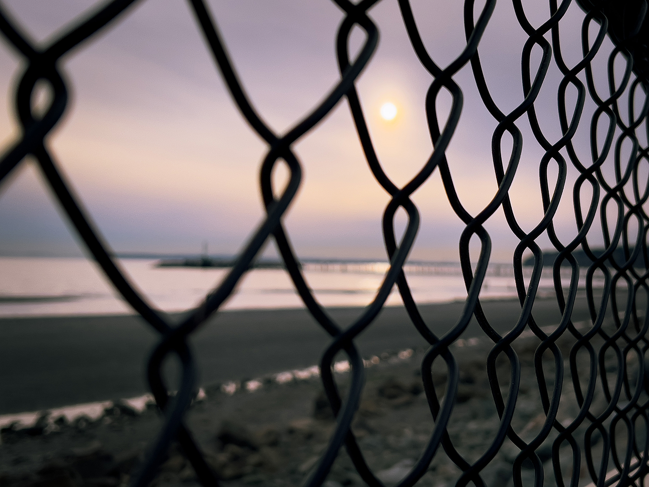 Close up of a chain link fence with a soft sunset beach blurred behind it