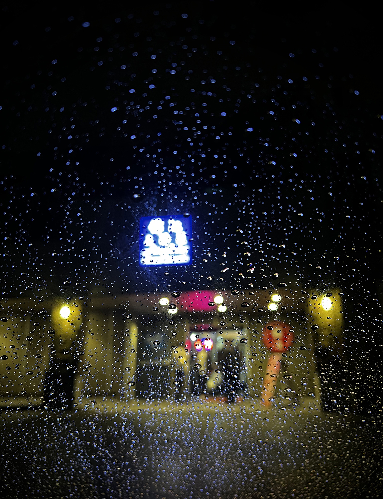Night view through a rain covered window of a building entrance lit by a glowing sign