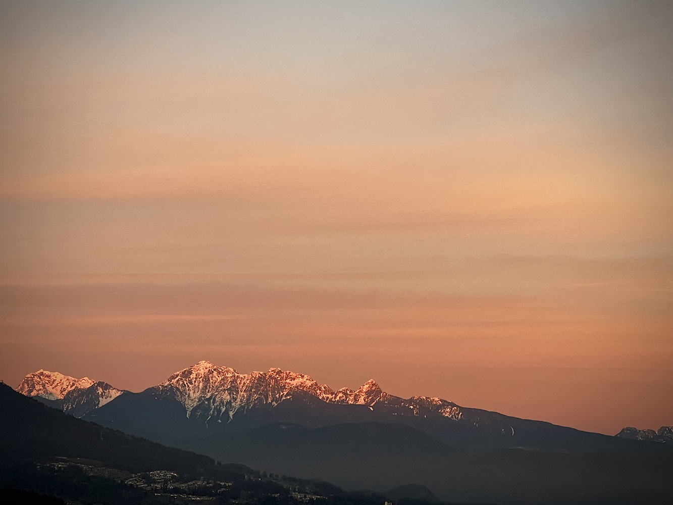 Snow capped mountains beneath a hazy peach coloured sky at dusk