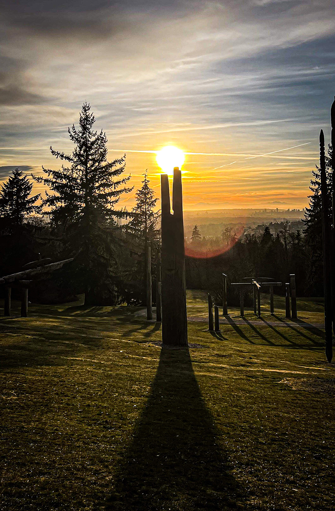 Sun glowing at the top of a tall post, casting a long shadow across a park lawn