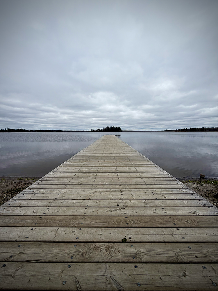 Wooden dock stretching out over calm grey water under an overcast sky