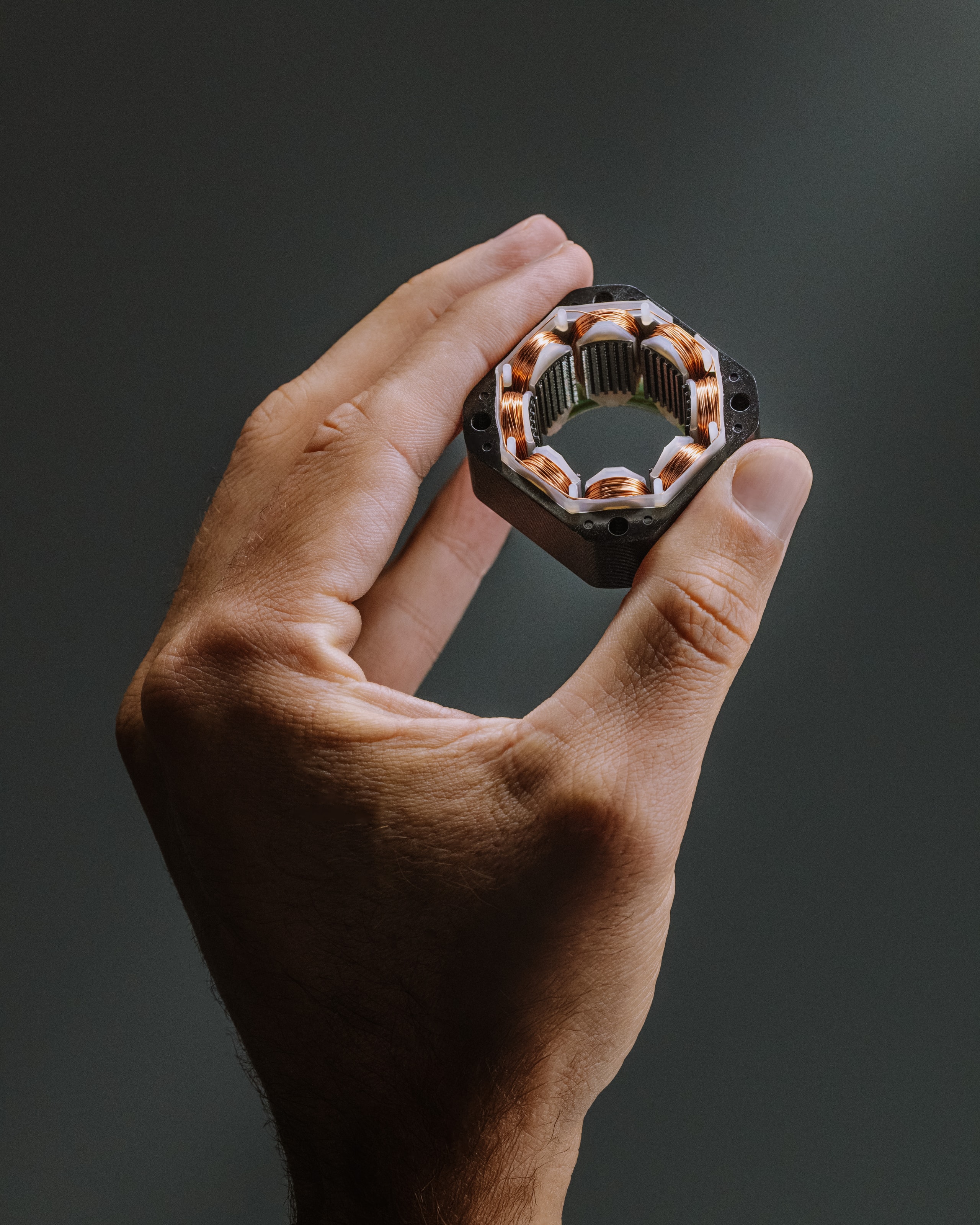 A single Smart Spring actuator held between finger and thumb, its copper windings visible