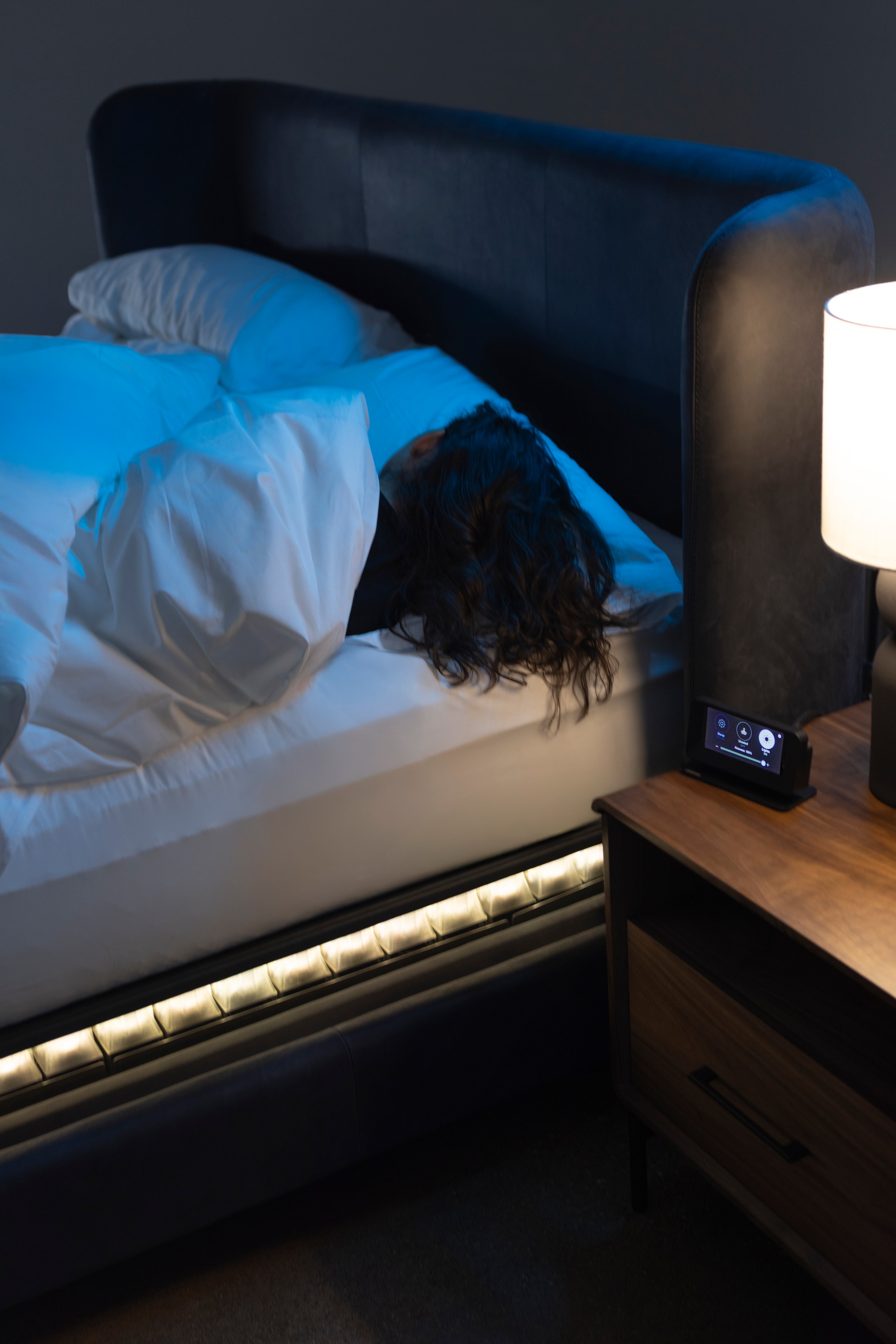 A sleeper asleep under white bedding with the bedside control lit beside them