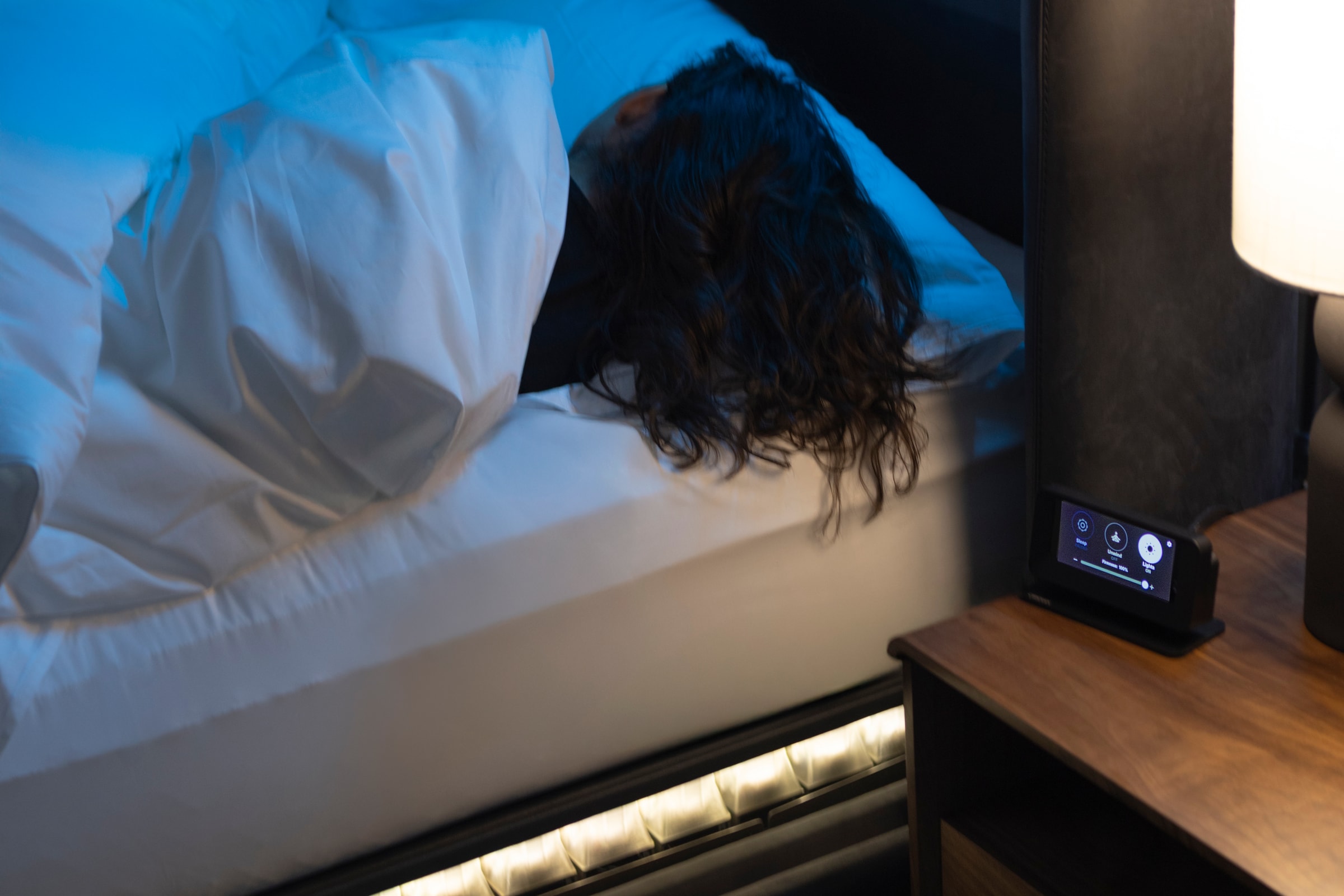 A sleeper asleep under white bedding with the bedside control lit beside them