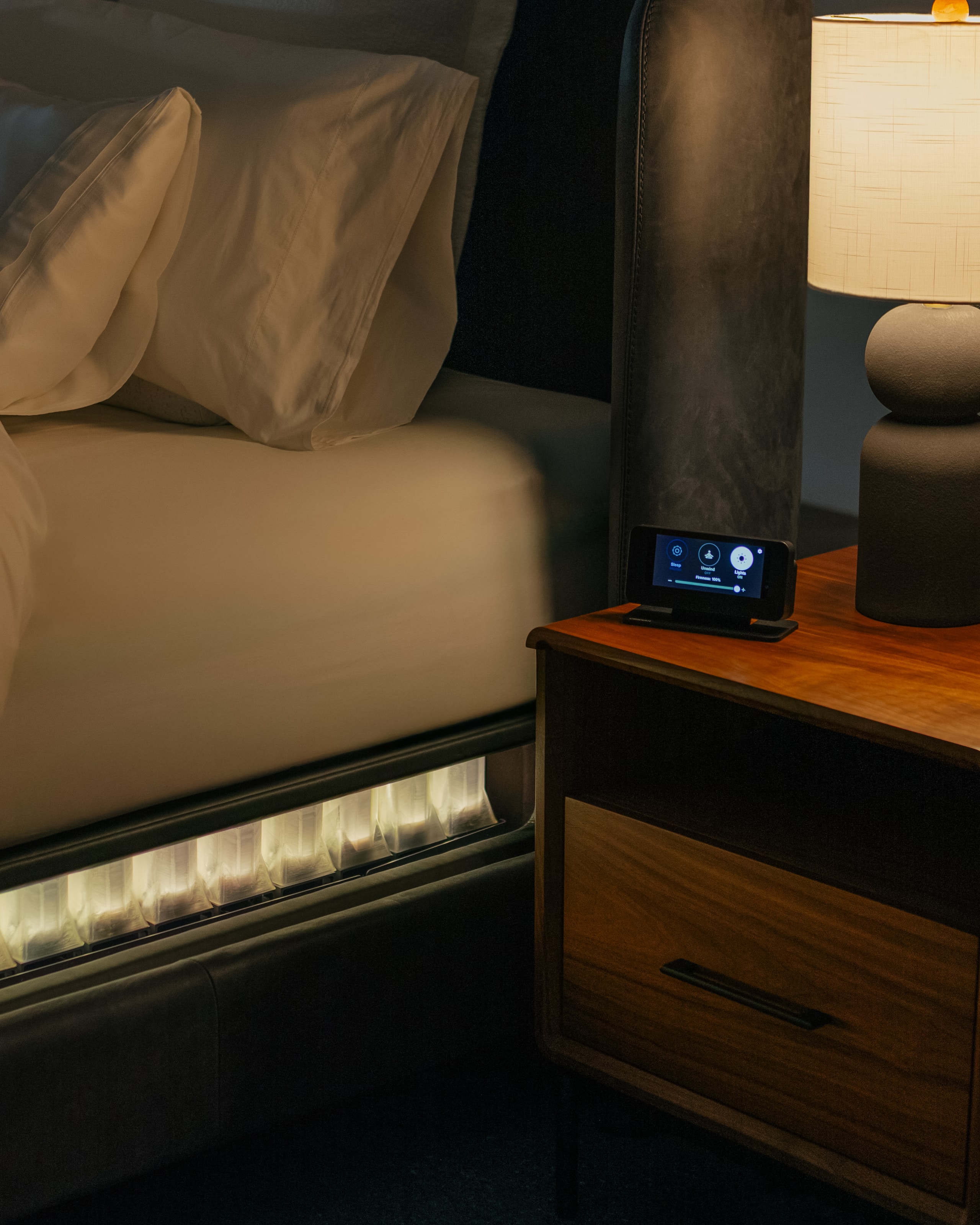 The bedside control beside the Sleep System at night, the spring base glowing below the sleep surface