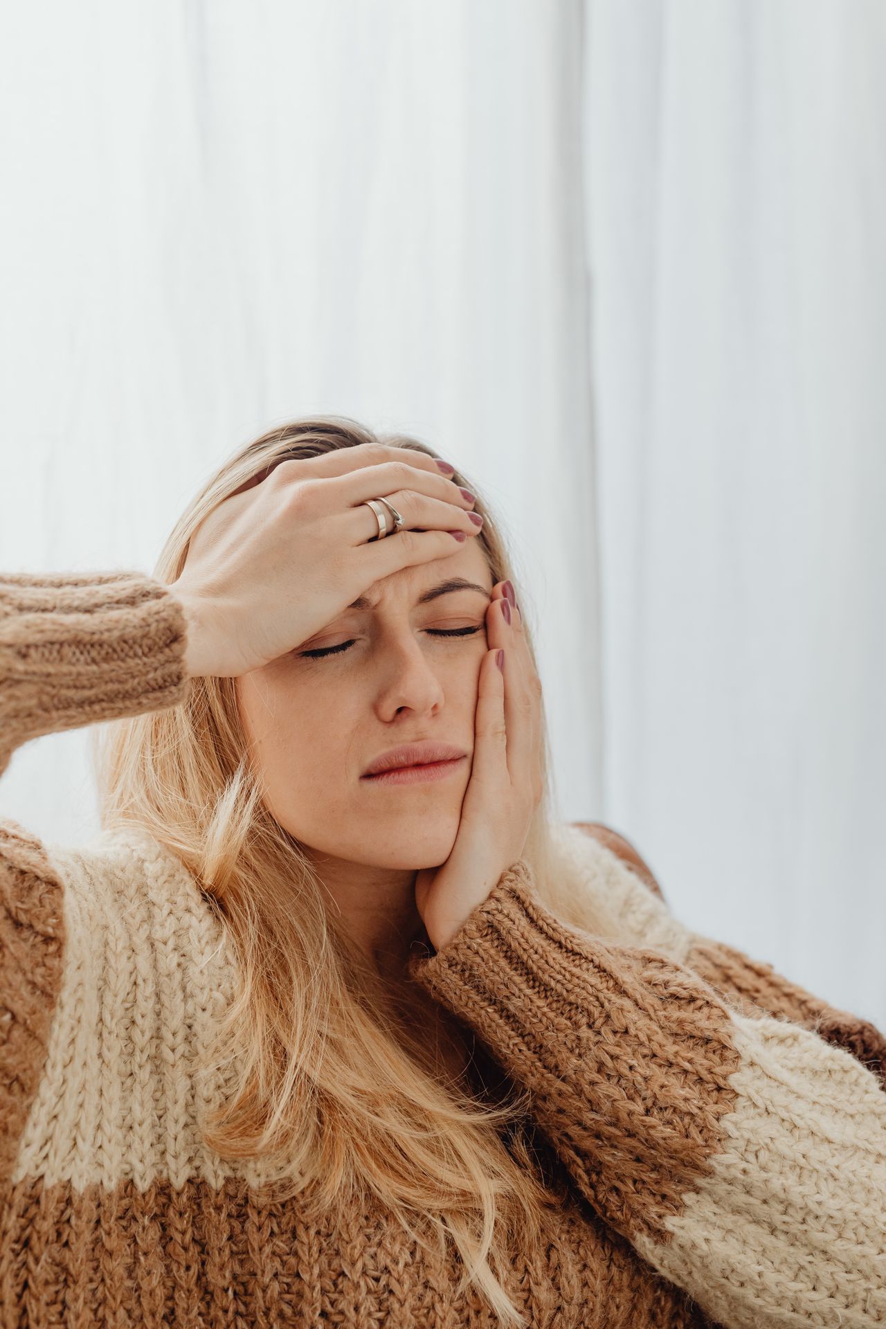 Woman holding her jaw and head from morning jaw pain, a common sign of TMJ or teeth grinding