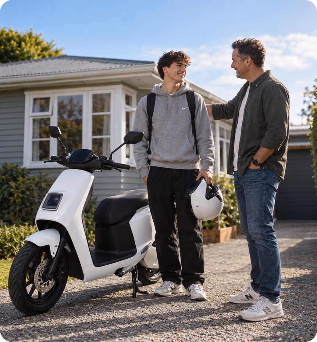 A young man in a gray hoodie and black pants holds a white helmet standing beside a white scooter while smiling at an older man in a dark green shirt and jeans outside a house.