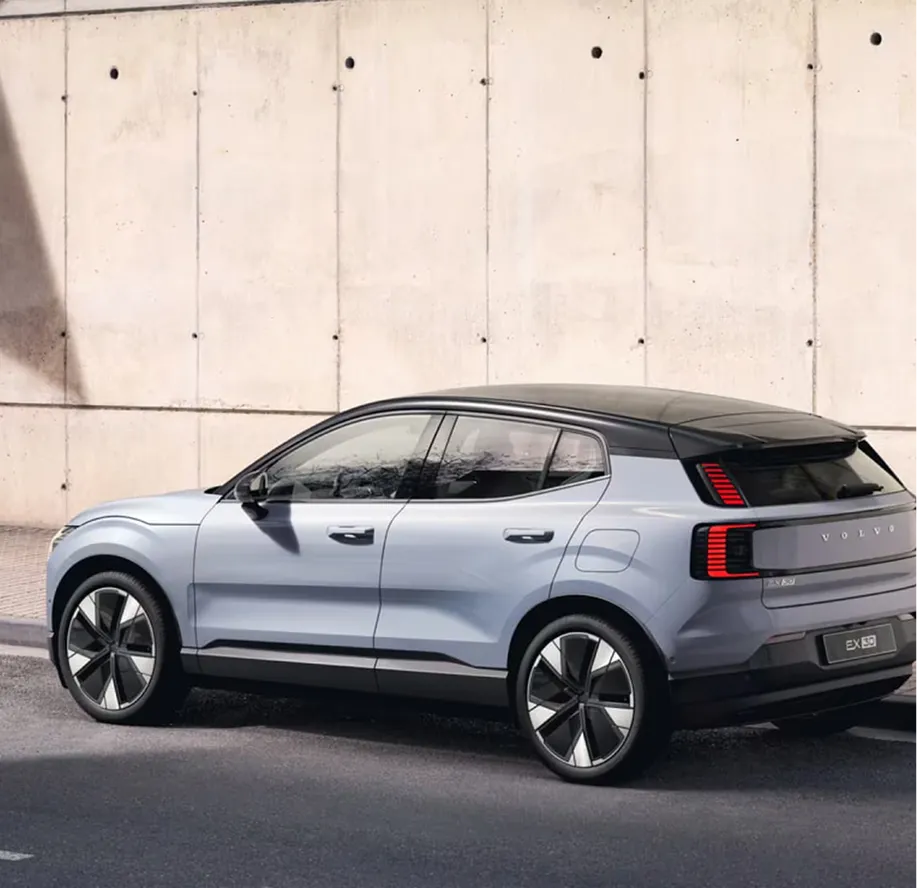 Rear three-quarter view of a light blue Volvo EX30 electric SUV parked against a concrete wall.