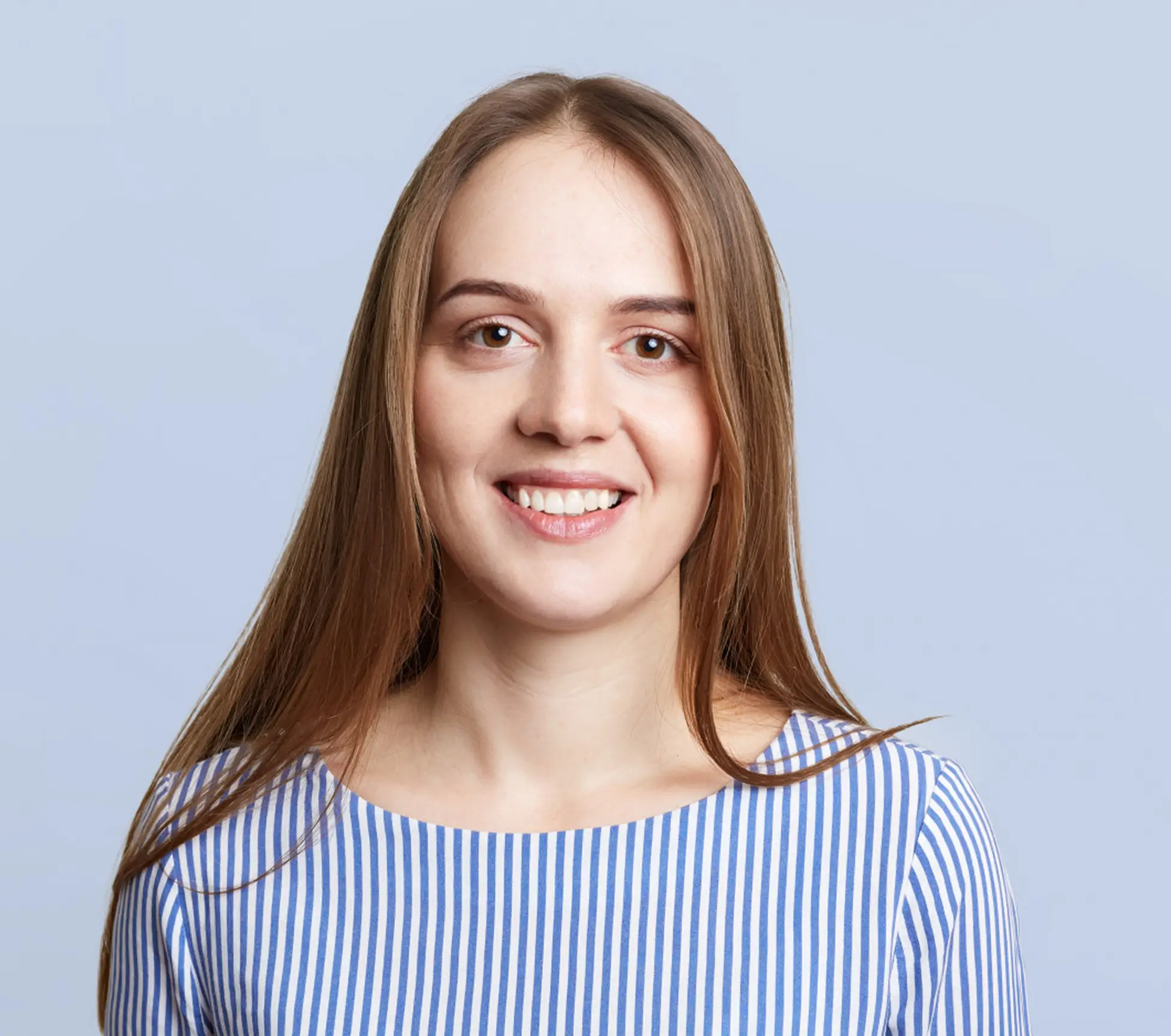 Smiling young woman with long straight light brown hair wearing a blue and white striped top against a light blue background.