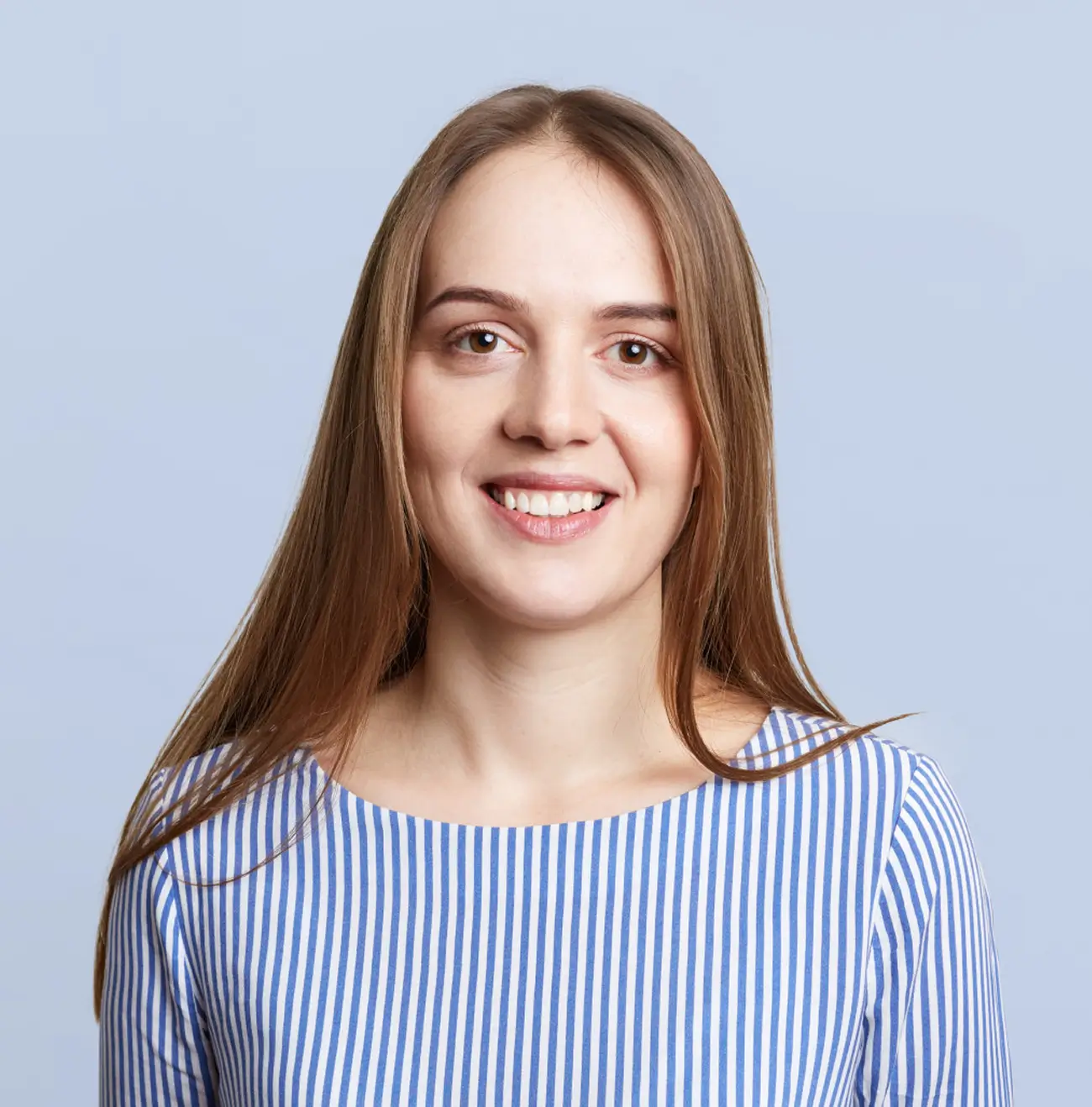 Young woman with straight light brown hair wearing a blue and white vertically striped top smiling against a light blue background.