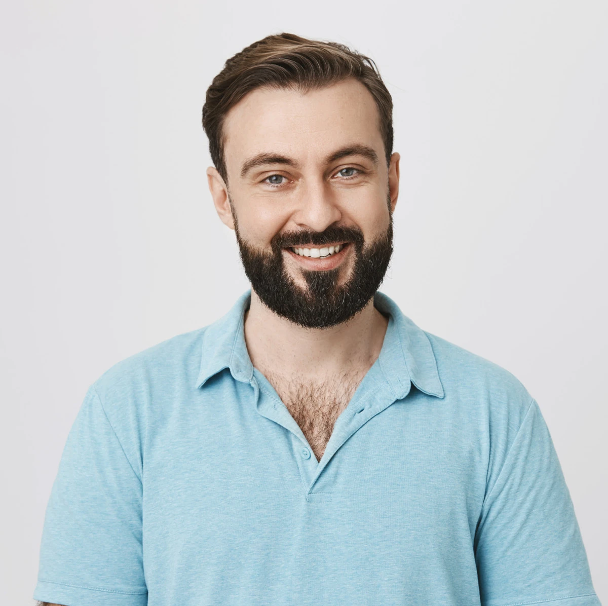 Portrait of a smiling man with a beard and short brown hair wearing a light blue polo shirt against a plain white background.