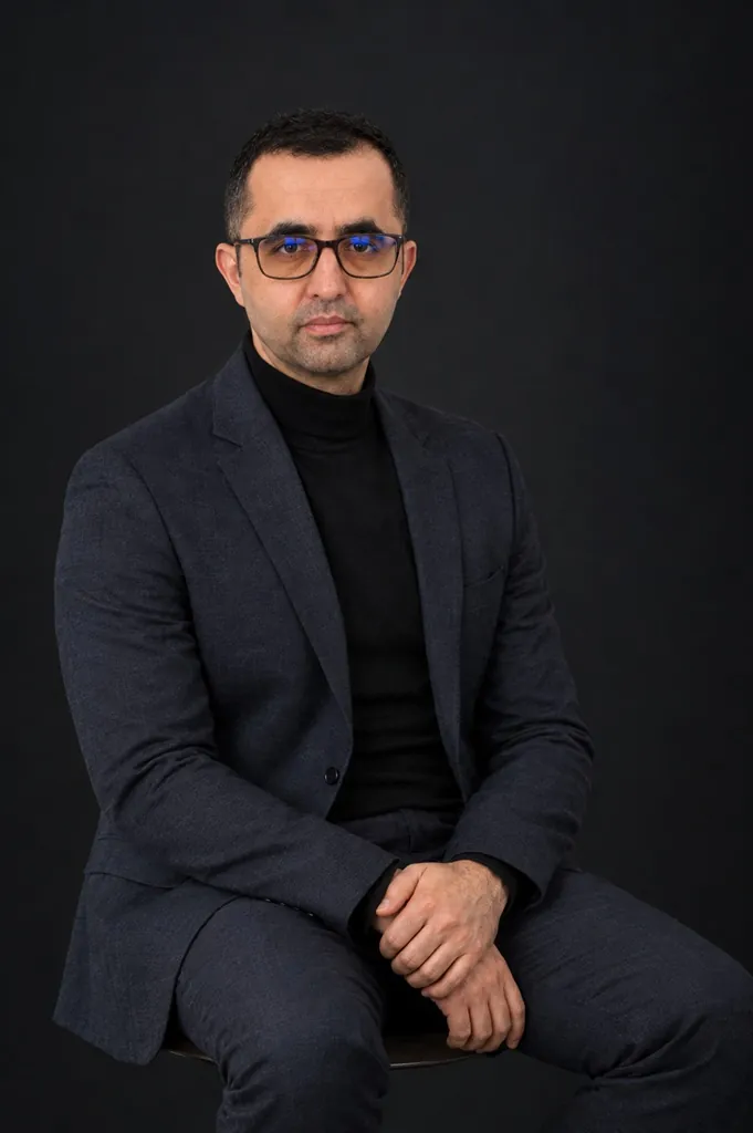 Portrait of Nesar, founder of phi.studio, seated in a dark suit and black turtleneck