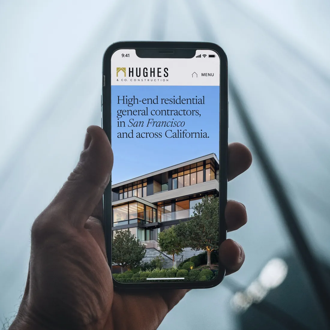 Our Hughes & Co. redesign concept on an iPhone held up against a misty glass tower.